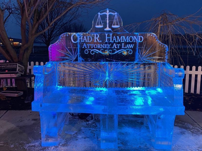 Ice sculpture of a bench with an attorney's name and scales of justice; lit with blue light.