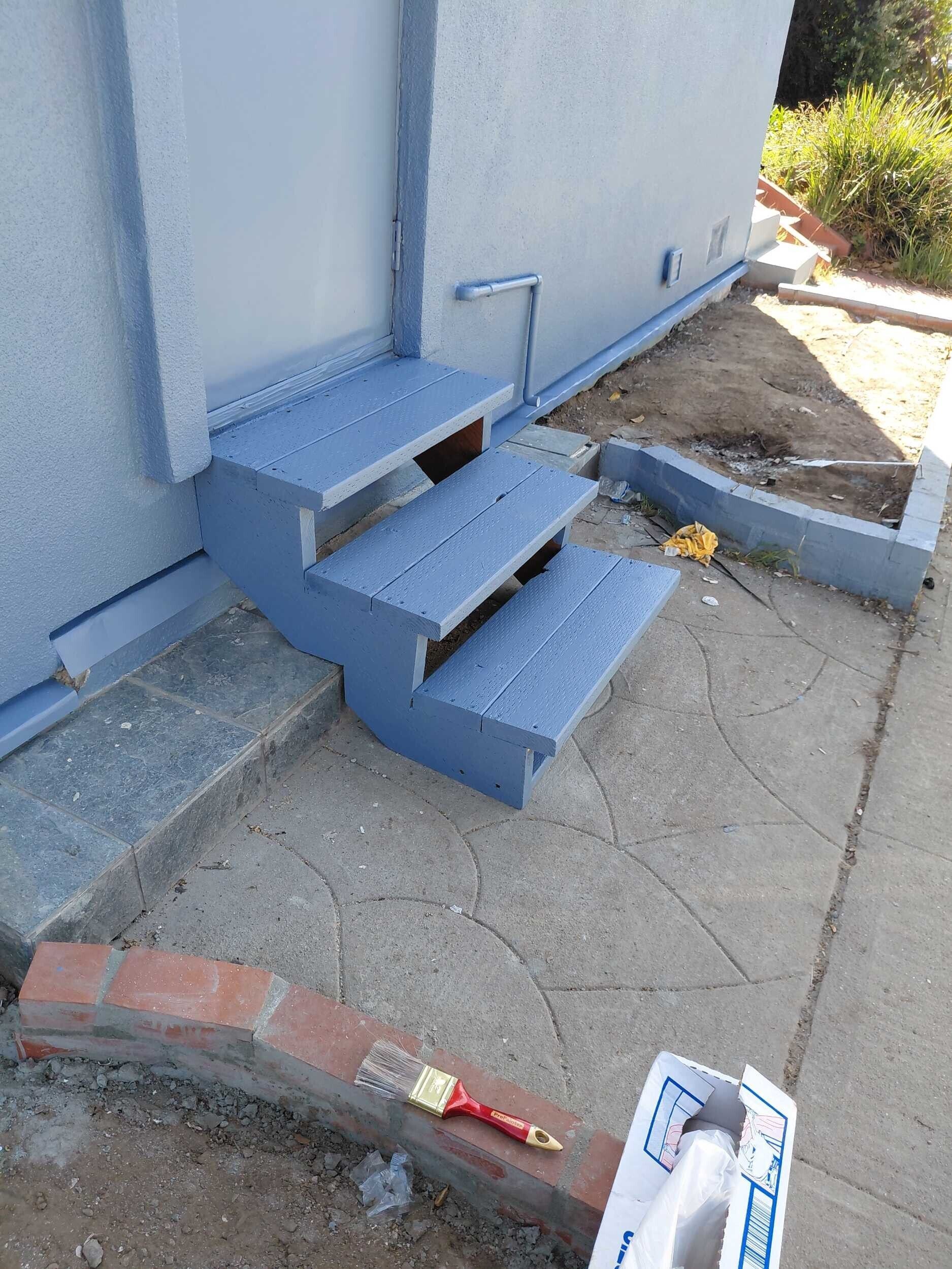 Exterior home repair project in progress by Dream Build Services, featuring damaged stucco removal, stair repair, new brick retaining wall installation, and fresh blue exterior paint. Sidewalk cleanup and entryway upgrade underway to improve curb appeal and structural safety. Bay Area residential construction and renovation.