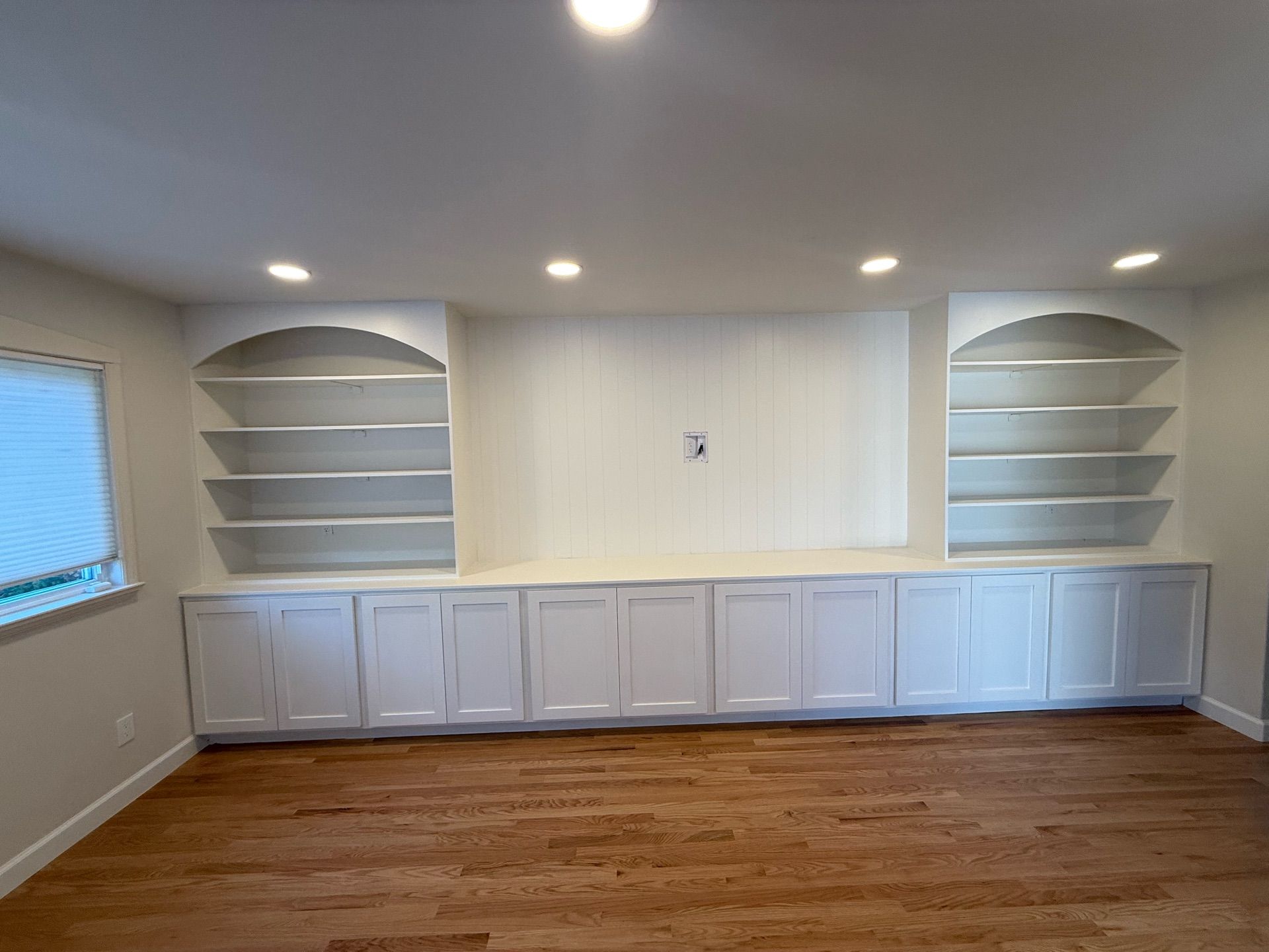 Built-in white cabinetry with open shelving and lower cabinets on either side of a central wall space with recessed lighting.