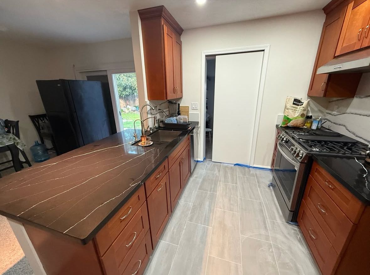 A kitchen with cherry cabinets, dark granite countertops, and stainless steel appliances. An island sits in the center, and a door leads to the outside.