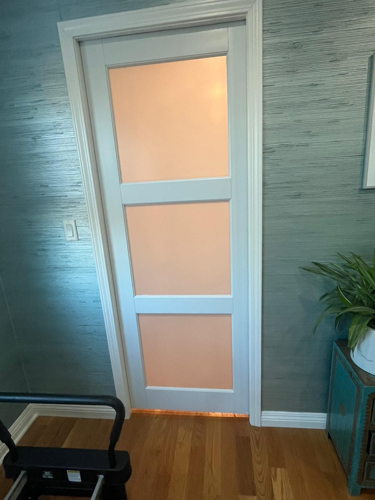 A door with three pieces of glass on it is in a room with hardwood floors.