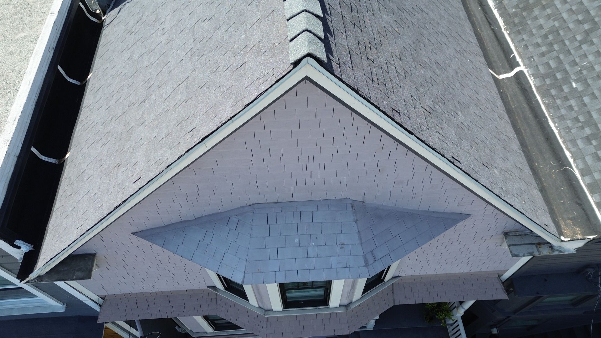 Overhead view of a dark gray slate roof with white trim, a triangular gable, and surrounding gutters.