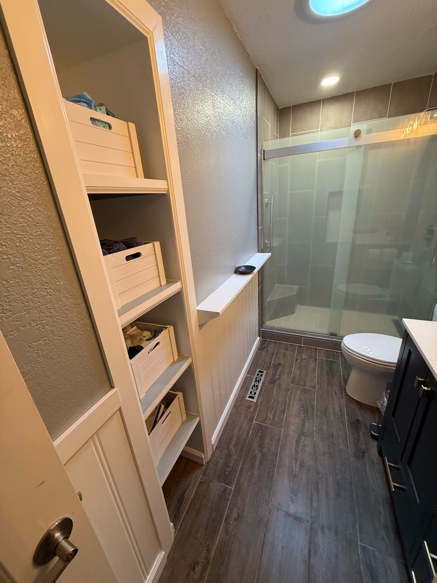 A bathroom with a toilet , sink , shelves and a skylight.