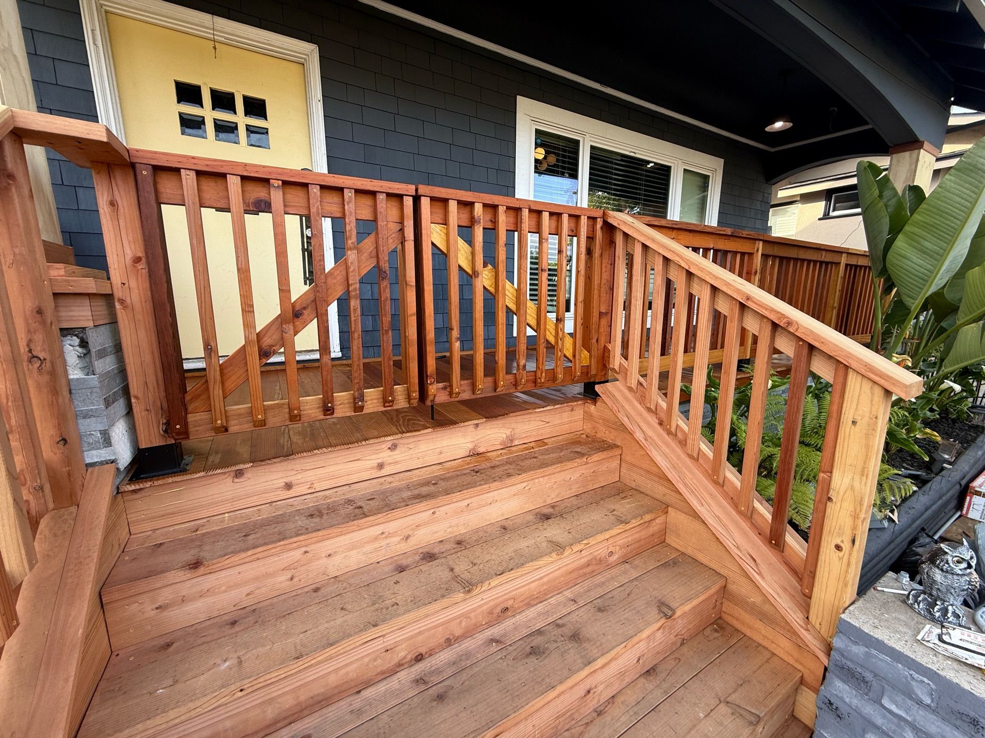Wooden steps and railing lead to a porch with a gate, painted dark gray siding, and a yellow door.