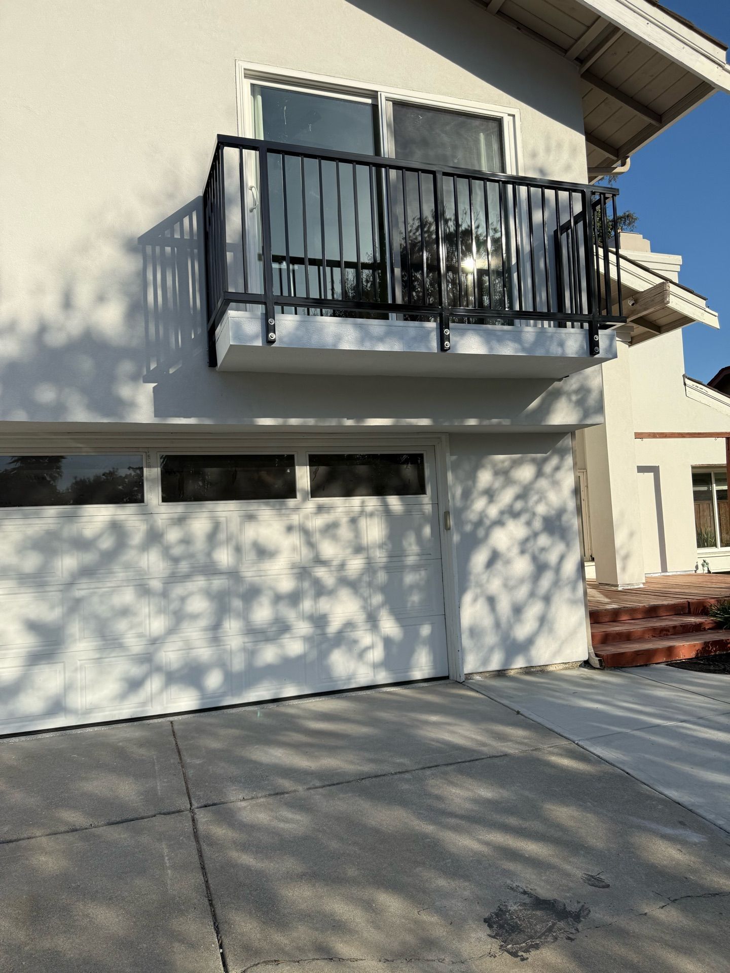 A white house with a balcony over the garage door.