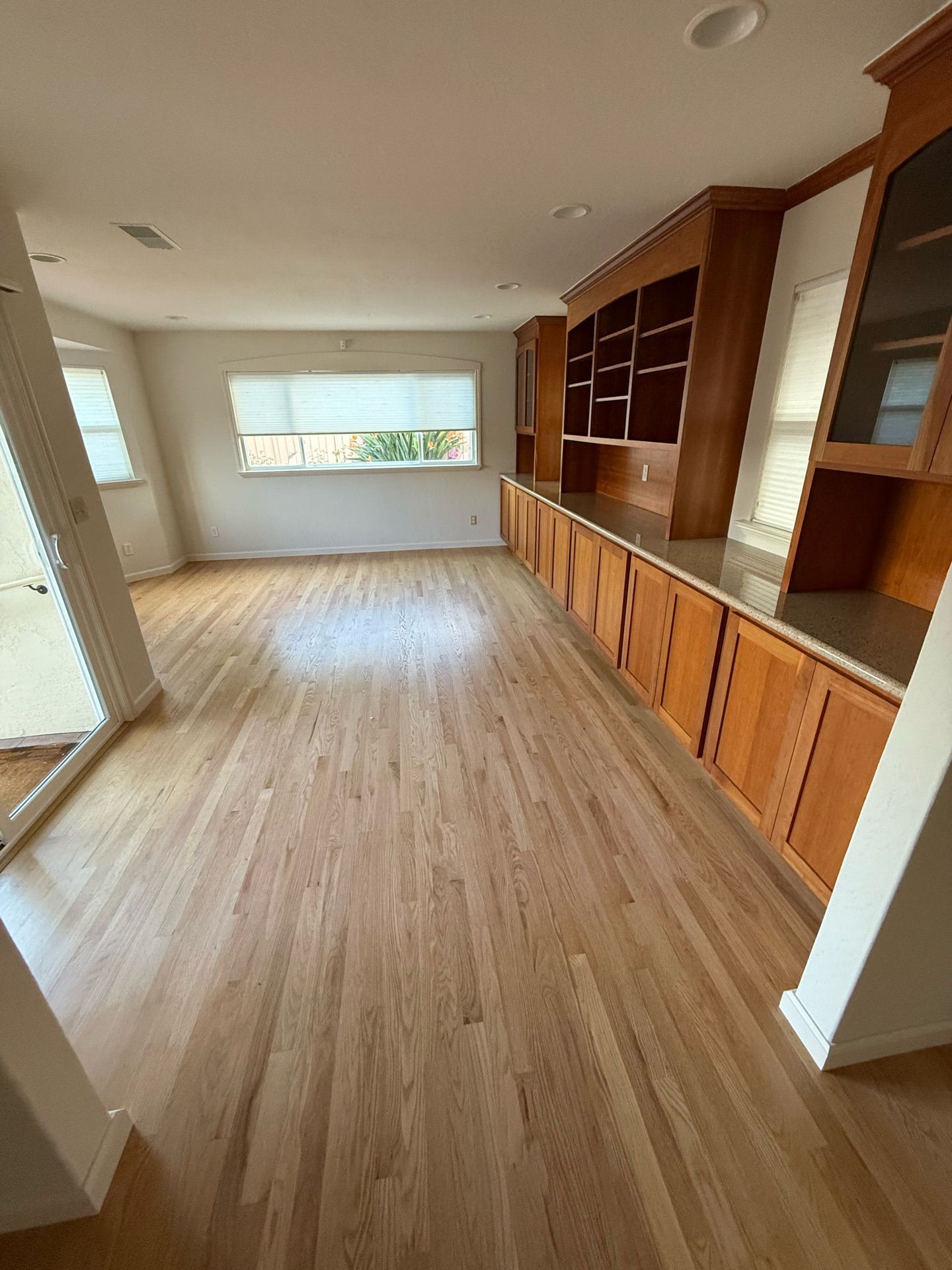 Light-filled room with hardwood floors, built-in wooden cabinets, and a window with a view.