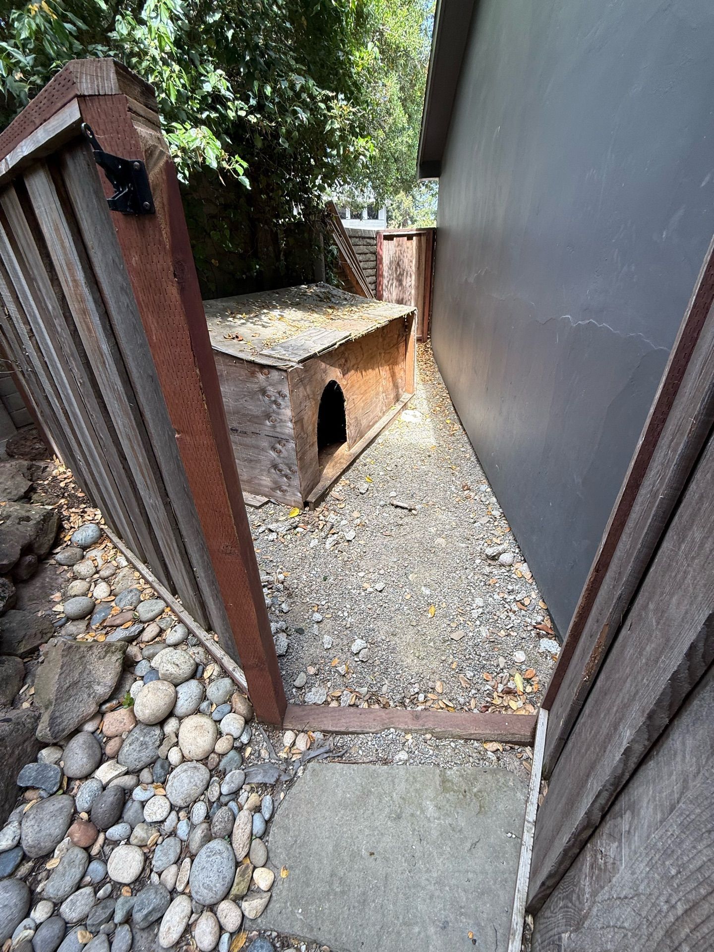 A dog house is behind a wooden fence in a backyard.