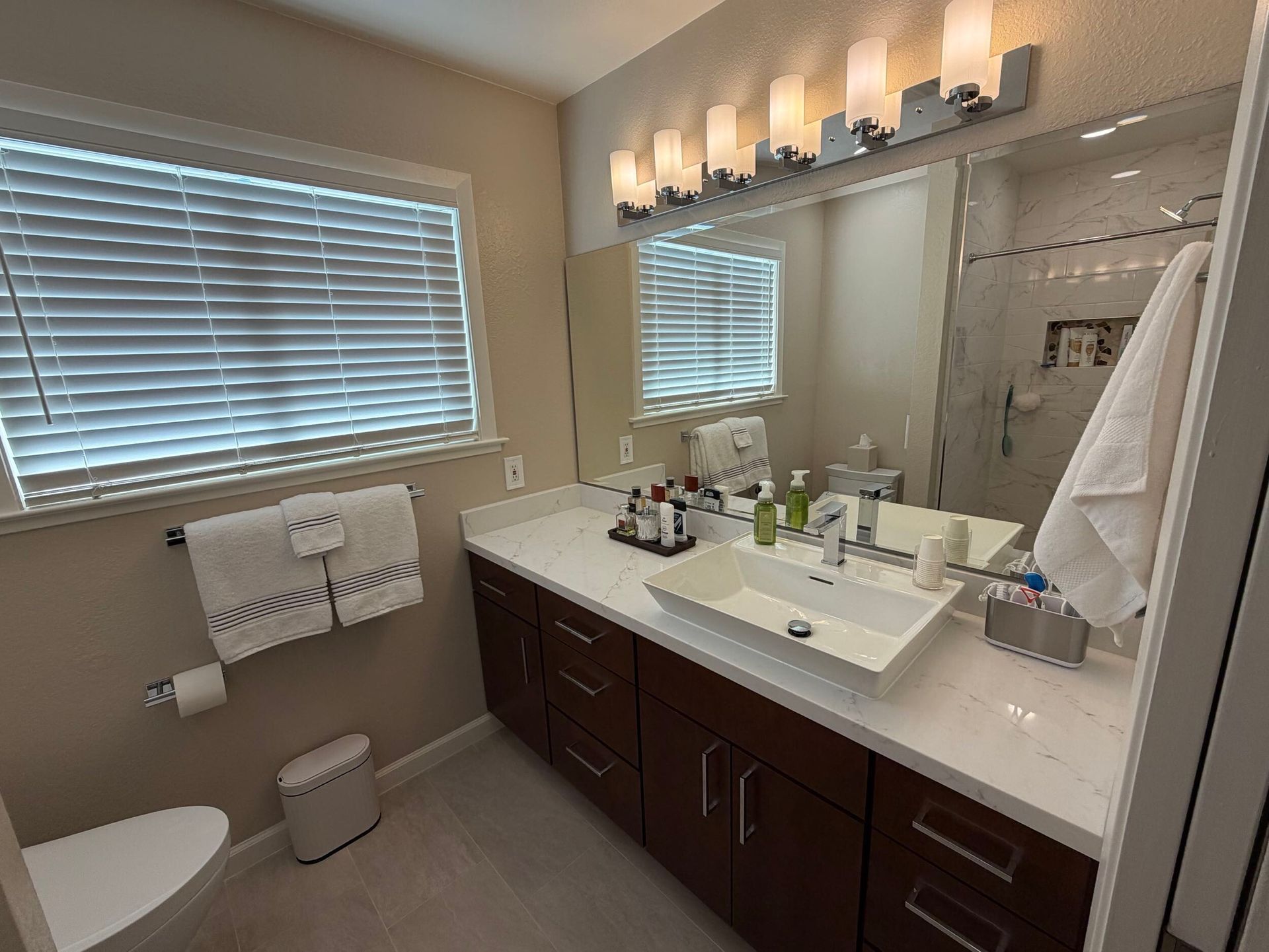 Updated bathroom remodel showcasing a modern walk-in shower with marble-style wall tile, pebble stone shower flooring, upgraded vanity with quartz countertop, contemporary sink and faucet, new lighting, and neutral color palette. Bathroom renovation completed by Dream Build Services, a residential remodeling contractor serving homeowners with bathroom and home renovation projects in the Bay Area.