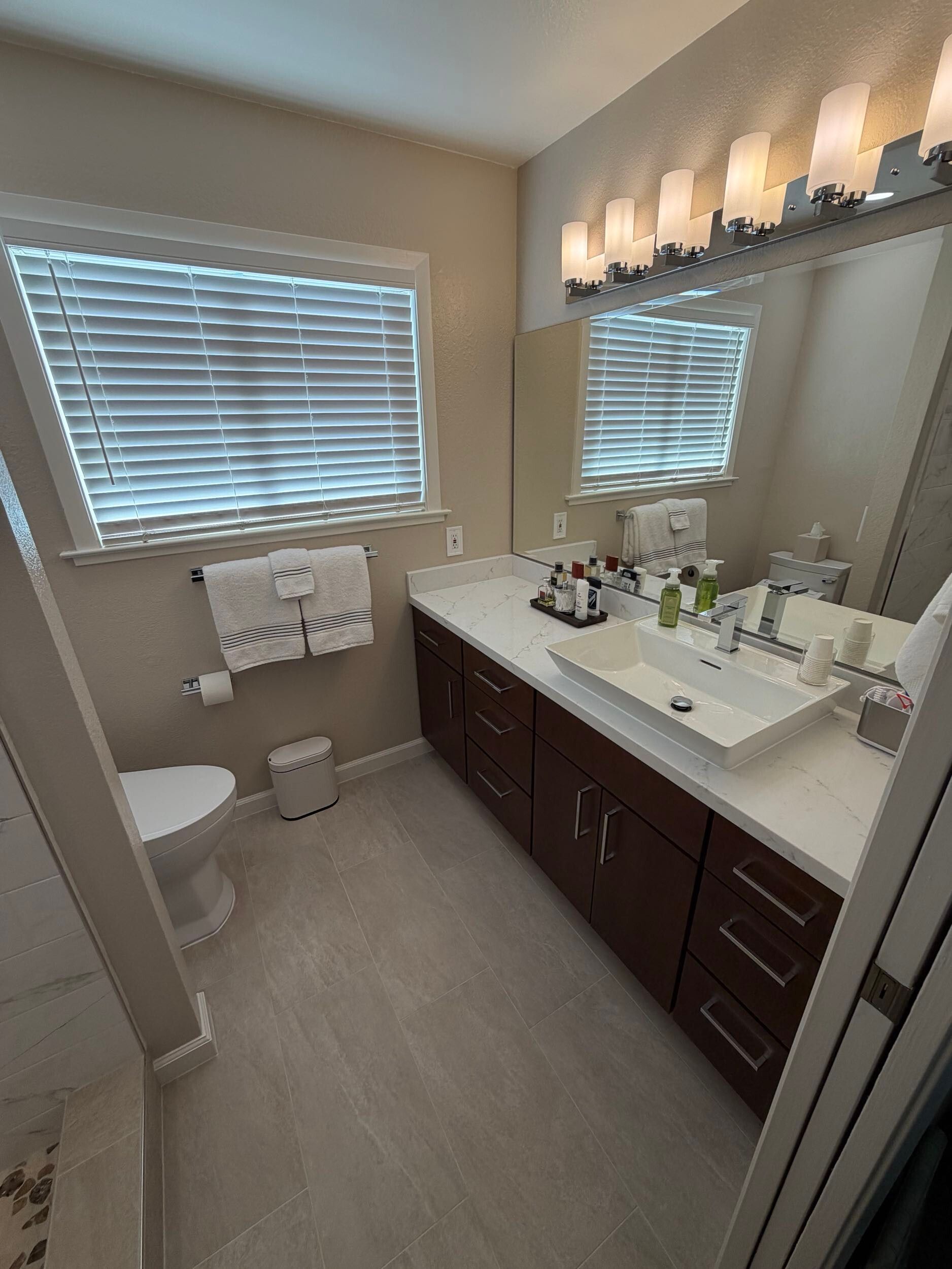 Updated bathroom remodel showcasing a modern walk-in shower with marble-style wall tile, pebble stone shower flooring, upgraded vanity with quartz countertop, contemporary sink and faucet, new lighting, and neutral color palette. Bathroom renovation completed by Dream Build Services, a residential remodeling contractor serving homeowners with bathroom and home renovation projects in the Bay Area.