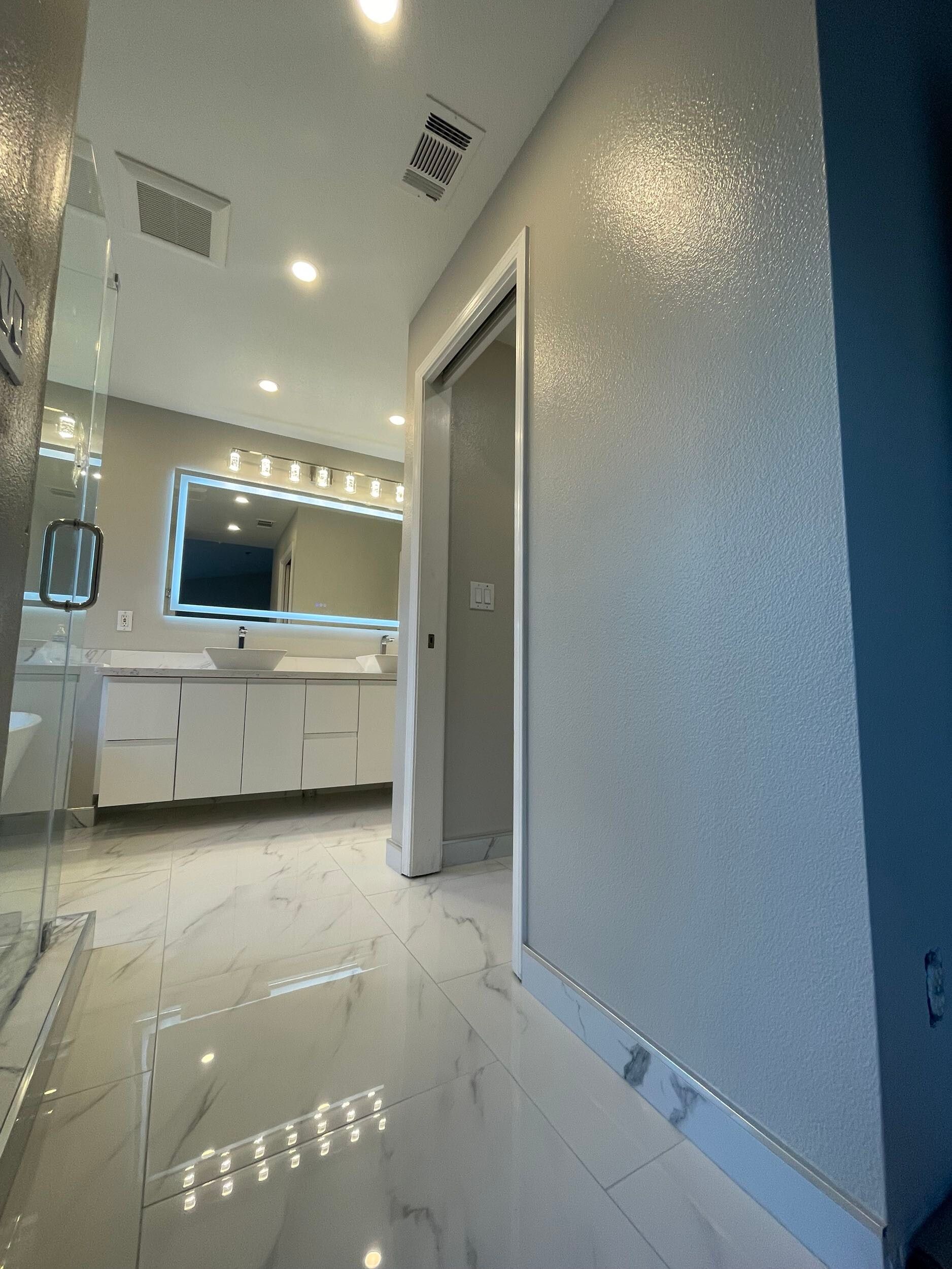 Luxury master bathroom remodel featuring a freestanding soaking tub by a large picture window, dual vessel sinks on a sleek white vanity, illuminated LED backlit mirror, recessed lighting, marble-look porcelain flooring, and frameless glass shower — custom design by Dream Build Services in the Bay Area.