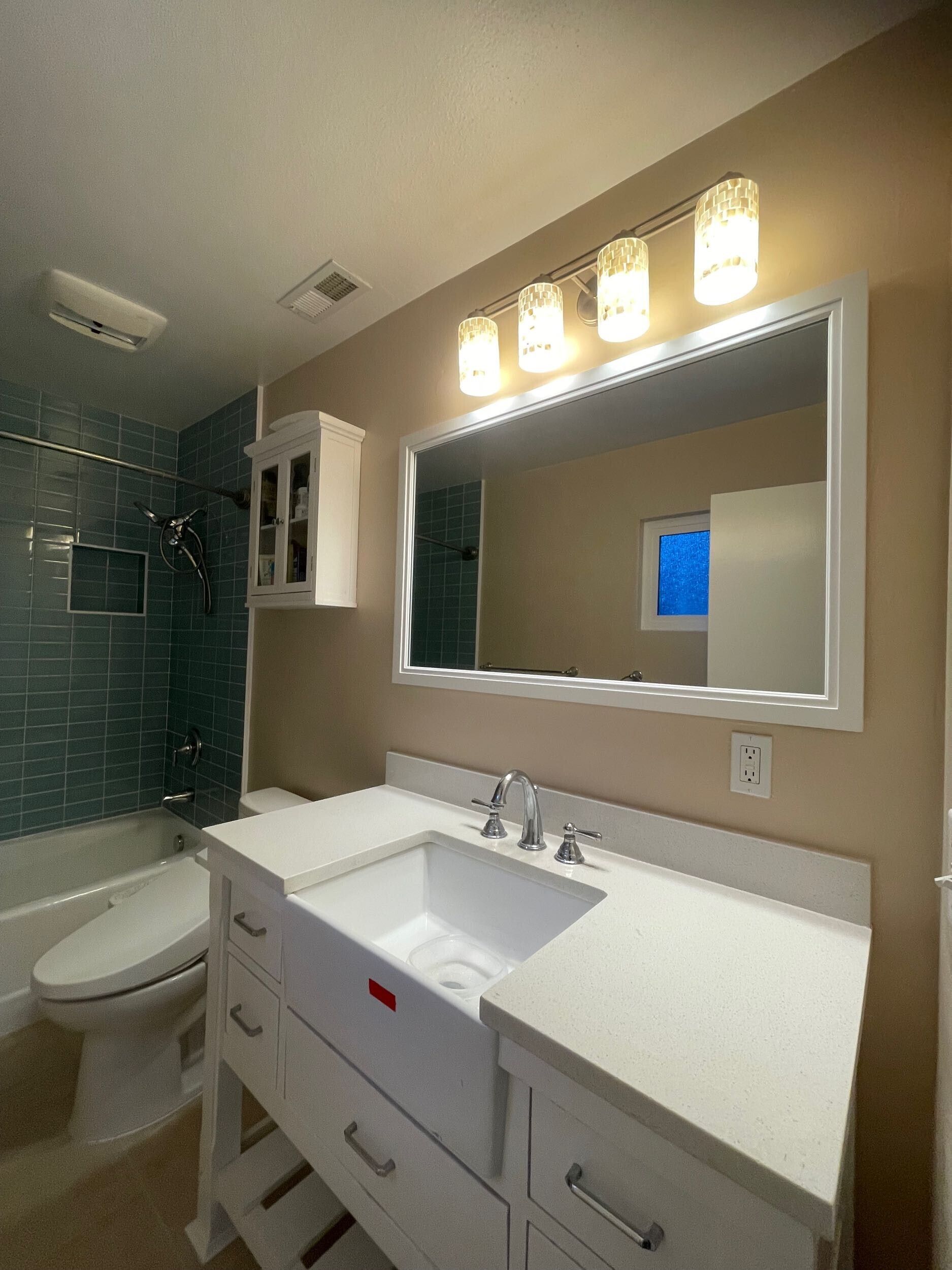 Complete bathroom remodel transformation showcasing before-and-after renovation. The updated space features a modern soaking tub with aqua subway tile walls, sleek white vanity with double sinks, bright lighting fixtures, and upgraded flooring. Project includes plumbing upgrades, custom tile shower niche, and improved storage with built-in cabinetry. Small bathroom remodel in the Bay Area with contemporary design and high-quality finishes by Dream Build Services.