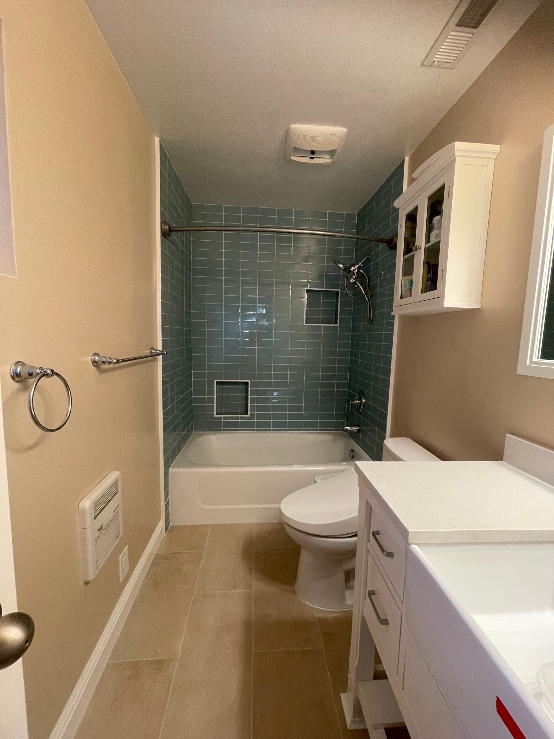 Complete bathroom remodel transformation showcasing before-and-after renovation. The updated space features a modern soaking tub with aqua subway tile walls, sleek white vanity with double sinks, bright lighting fixtures, and upgraded flooring. Project includes plumbing upgrades, custom tile shower niche, and improved storage with built-in cabinetry. Small bathroom remodel in the Bay Area with contemporary design and high-quality finishes by Dream Build Services.