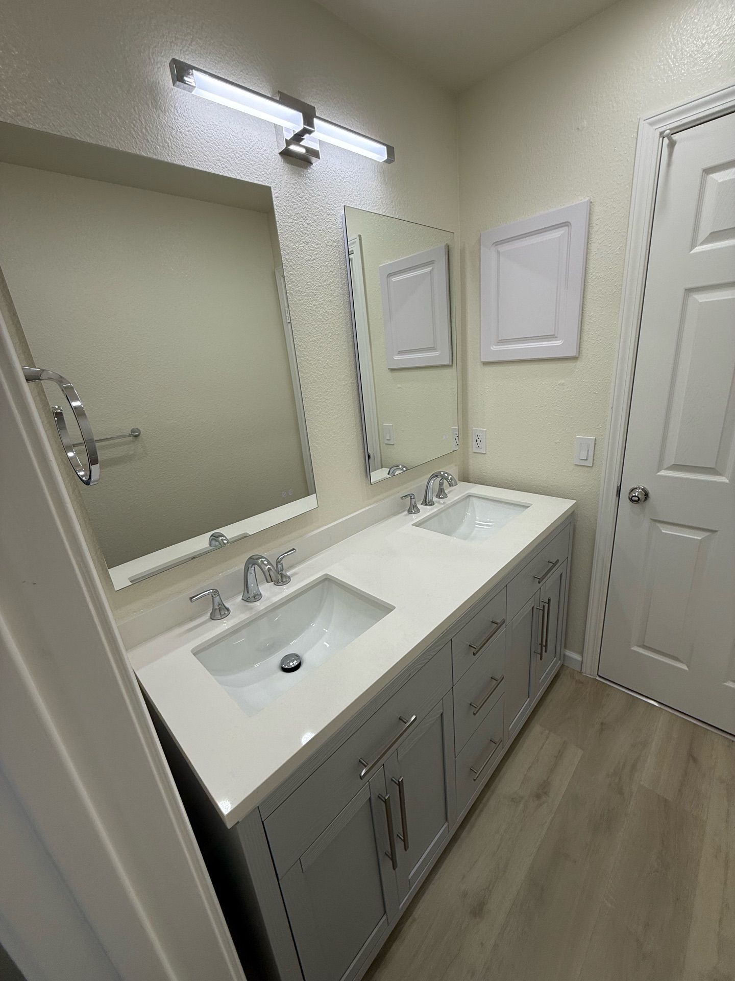 Bathroom with a double sink vanity, two mirrors, and a door. The vanity is gray with a white countertop.