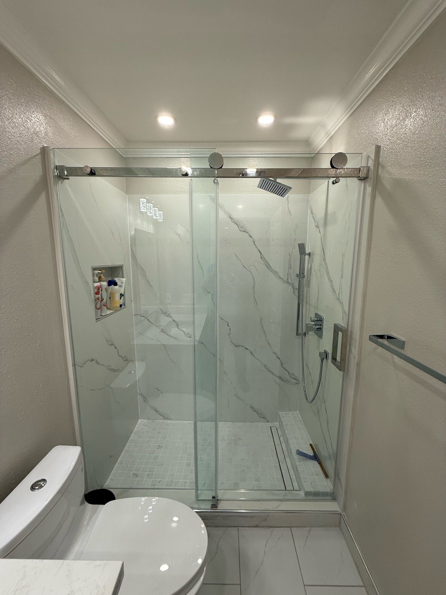 Contemporary bathroom remodel featuring a sleek white floating vanity with under-mount sink, frameless mirror with modern LED lighting, walk-in shower with glass sliding doors and marble-look porcelain tiles, and gray floor tiles with subtle veining — project by Dream Build Services in the Bay Area.