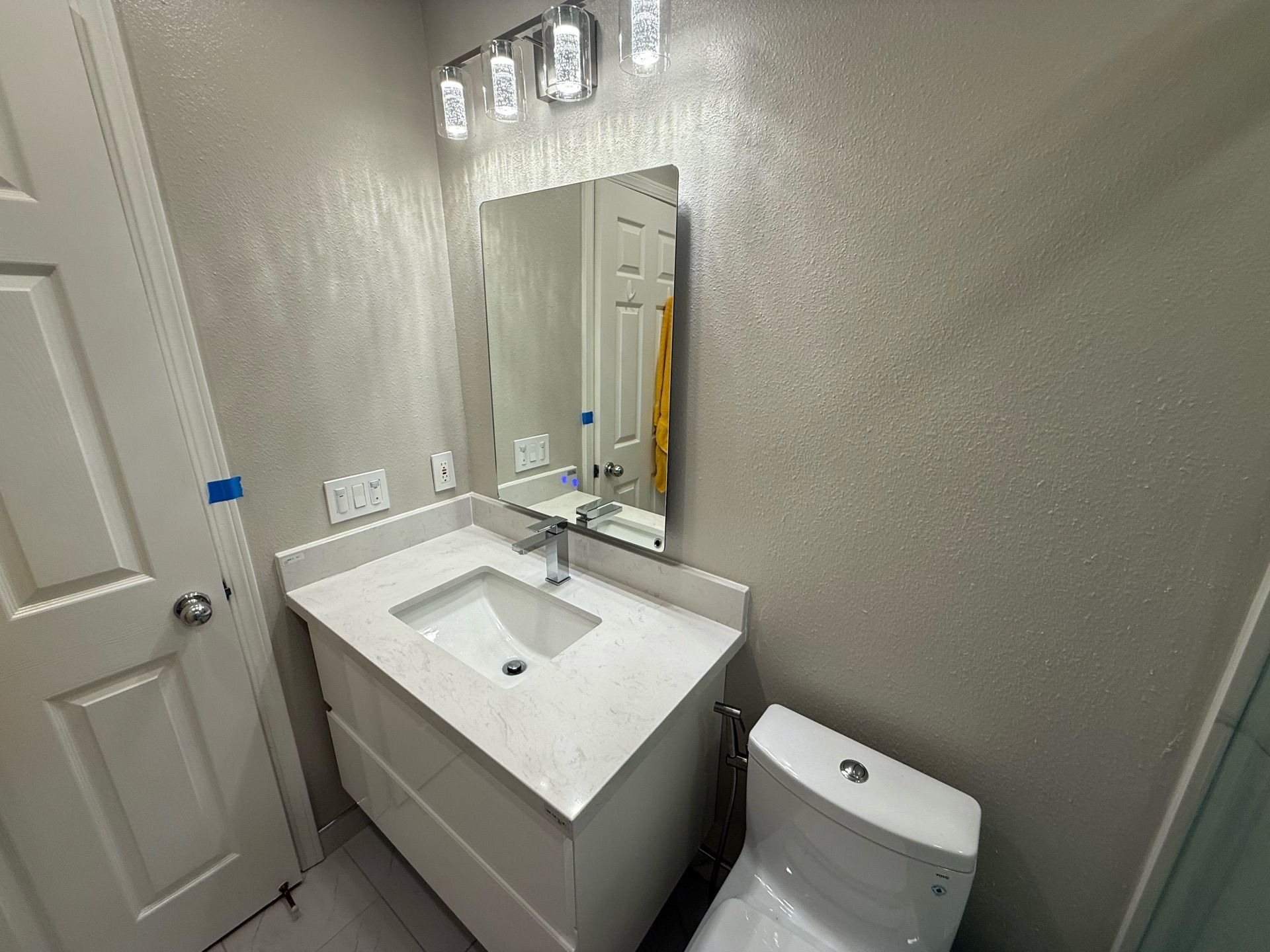 Contemporary bathroom remodel featuring a sleek white floating vanity with under-mount sink, frameless mirror with modern LED lighting, walk-in shower with glass sliding doors and marble-look porcelain tiles, and gray floor tiles with subtle veining — project by Dream Build Services in the Bay Area.