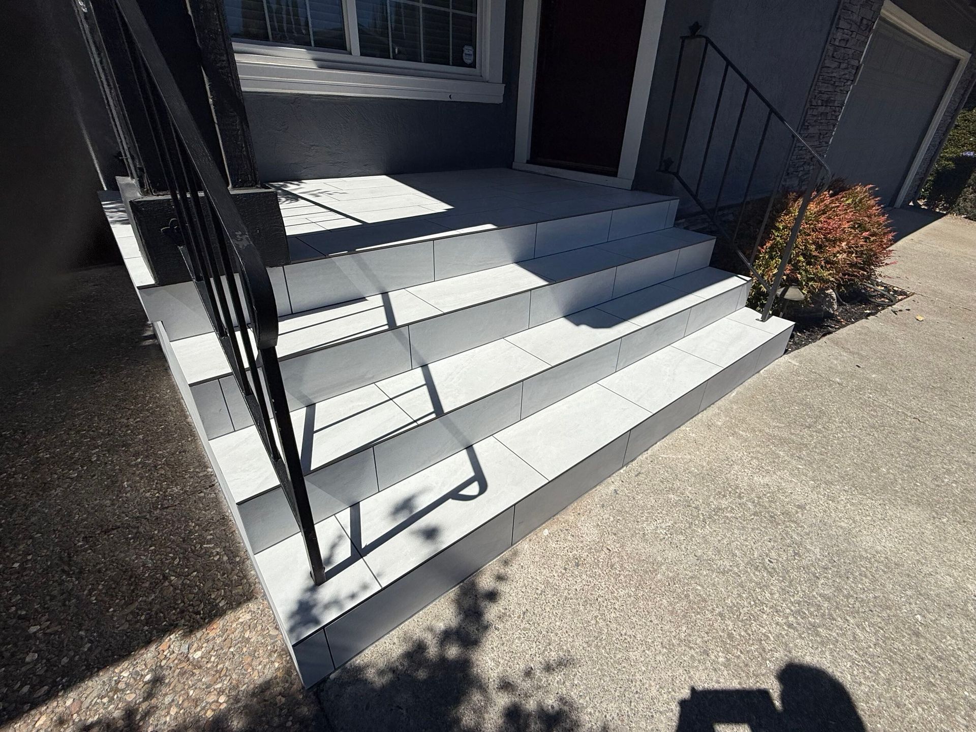 Modern front porch remodel featuring large-format light gray tile steps with black iron railings and a clean concrete landing – completed by Dream Build Services, Bay Area general contractor.