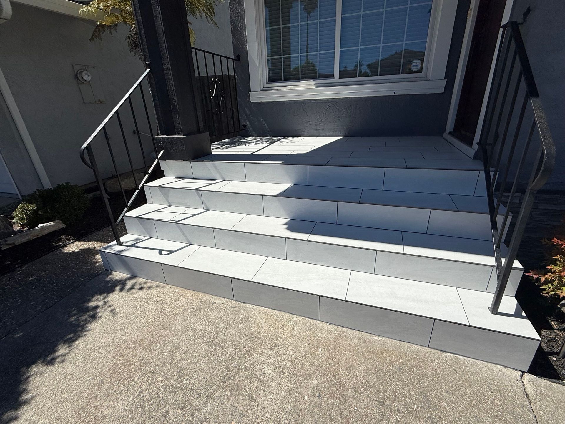Modern front porch remodel featuring large-format light gray tile steps with black iron railings and a clean concrete landing – completed by Dream Build Services, Bay Area general contractor.