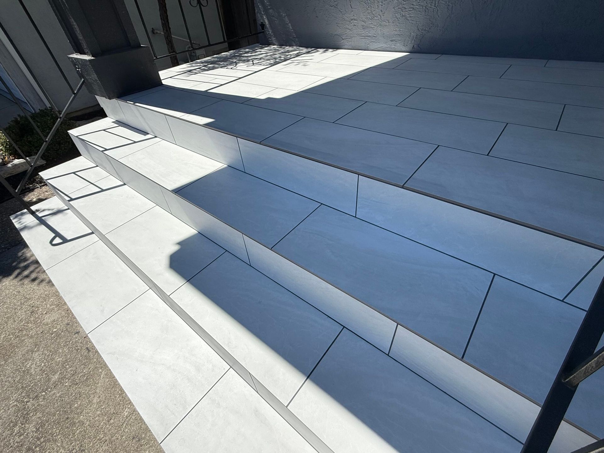 Modern front porch remodel featuring large-format light gray tile steps with black iron railings and a clean concrete landing – completed by Dream Build Services, Bay Area general contractor.