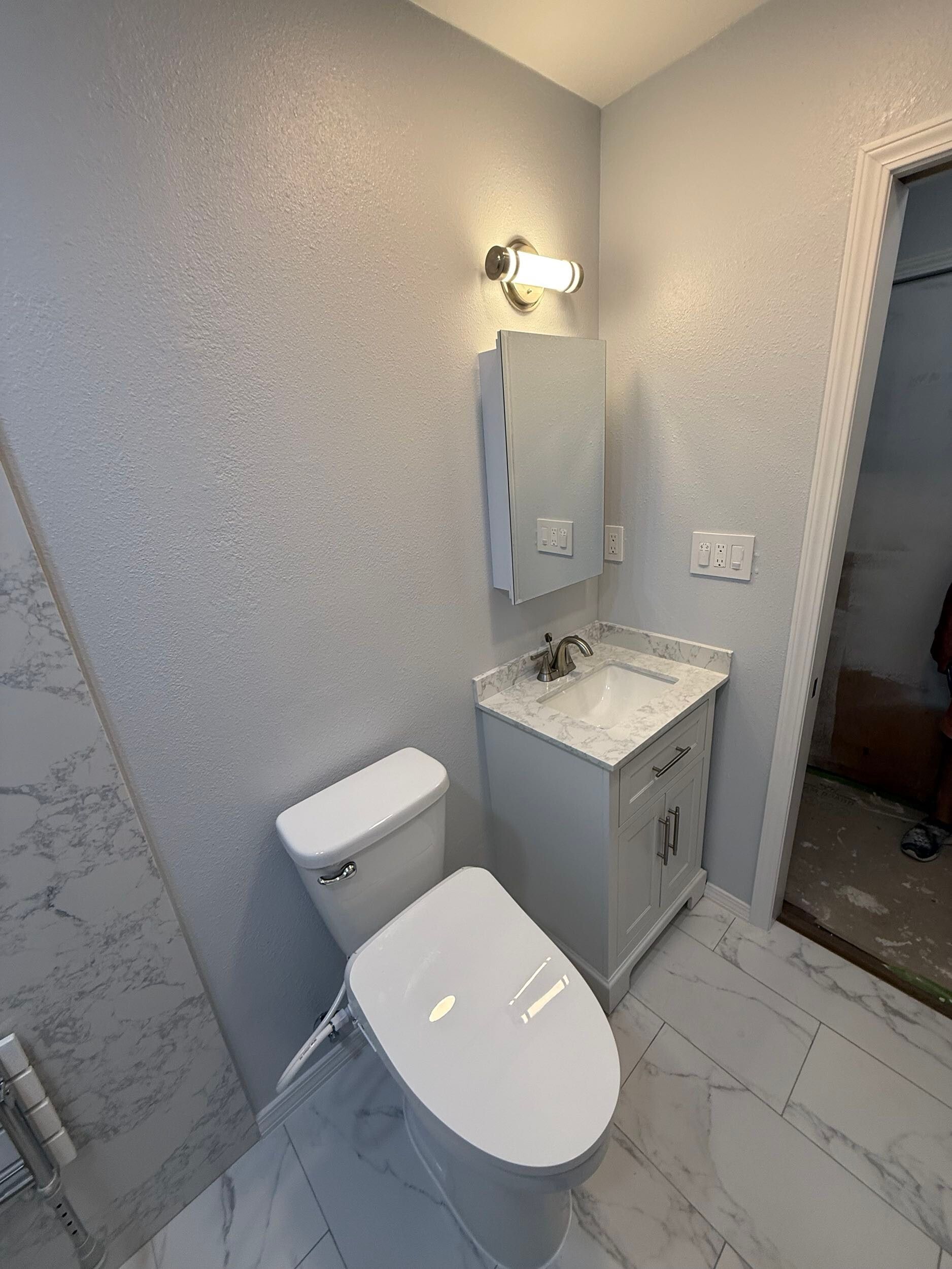 Modern bathroom remodel featuring white marble-style porcelain tiles on the floor and shower walls, walk-in shower with dual shower heads and accessibility grab bars, white vanity with under-mount sink and brushed nickel fixtures, completed by Dream Build Services in the Bay Area.