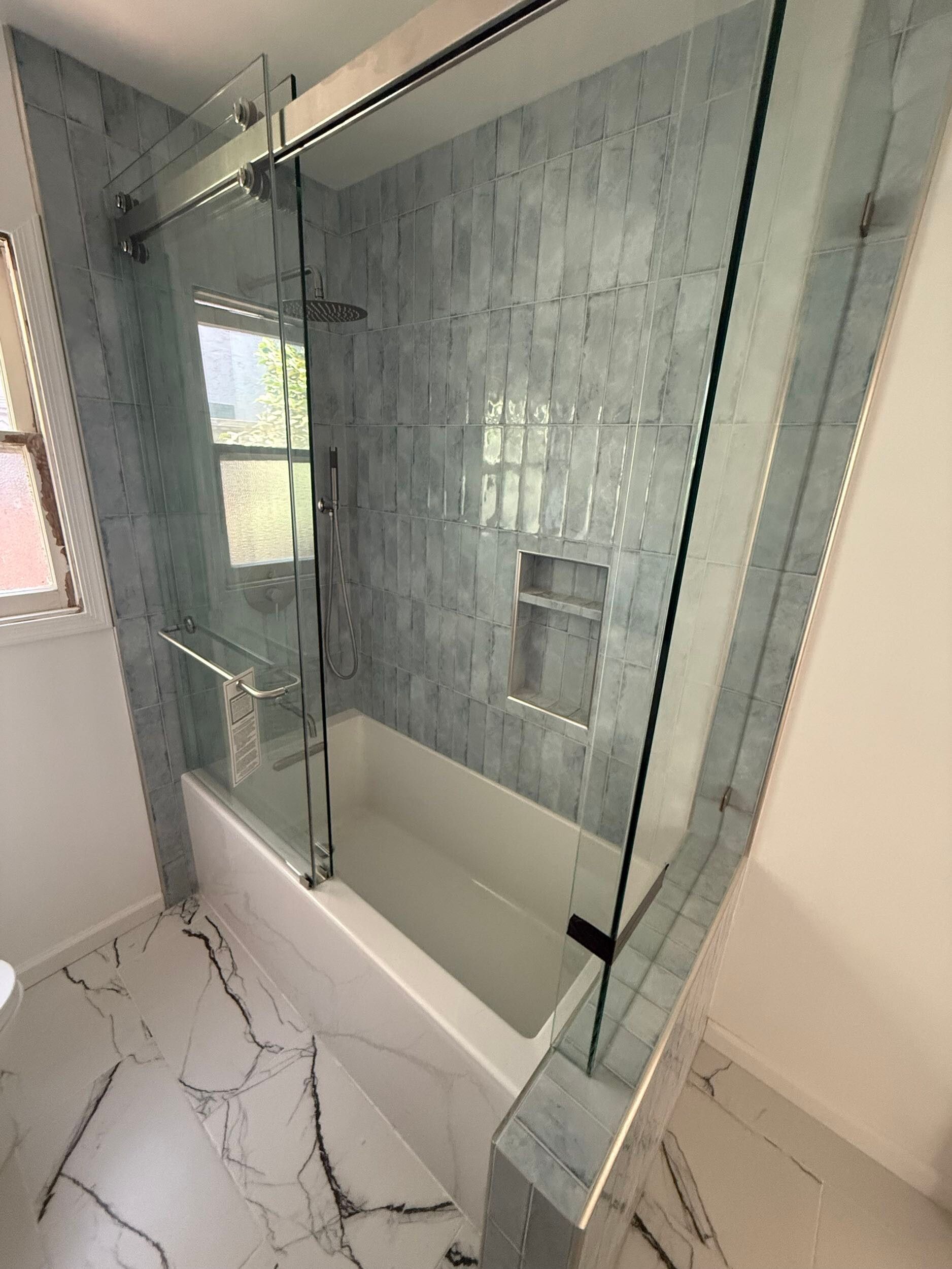 Modern bathroom remodel featuring a sleek floating vanity with quartz countertop, frameless LED mirror, and upgraded lighting fixtures. The shower area is designed with glass doors, rainfall showerhead, and elegant blue ceramic wall tiles for a spa-like feel. White marble-look porcelain floor tiles add a touch of luxury and durability. Perfect blend of contemporary design and functionality, ideal for homeowners in the Bay Area looking for stylish bathroom renovation ideas.