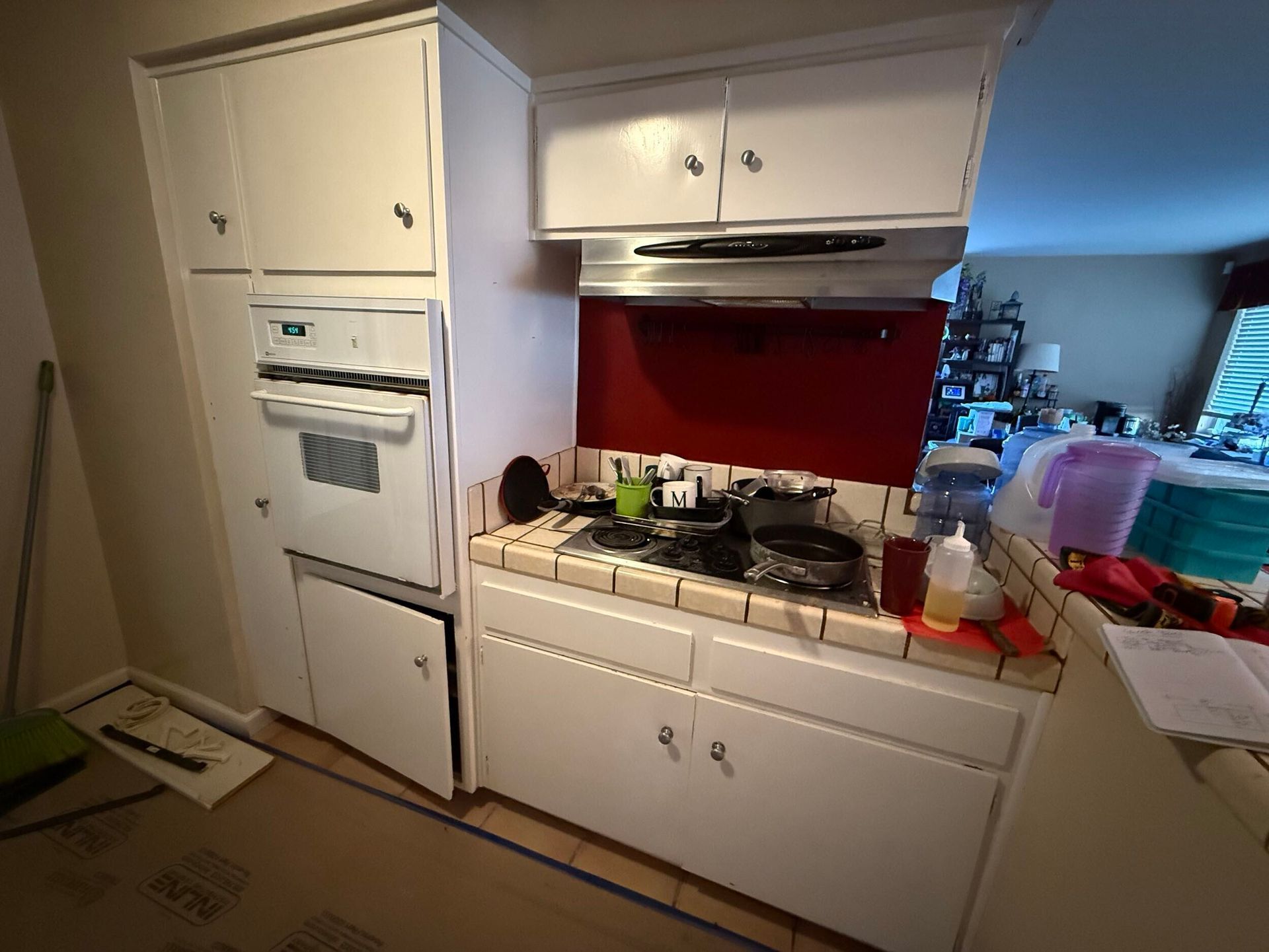 Modern kitchen remodel featuring gray shaker-style lower cabinets, white upper cabinets, quartz countertops with subtle veining, stainless steel appliances, built-in oven, sleek black cooktop, contemporary range hood, and textured stone tile backsplash. Renovation completed by Dream Build Services, showcasing high-quality craftsmanship, modern design, and functional layout for residential kitchen remodeling.