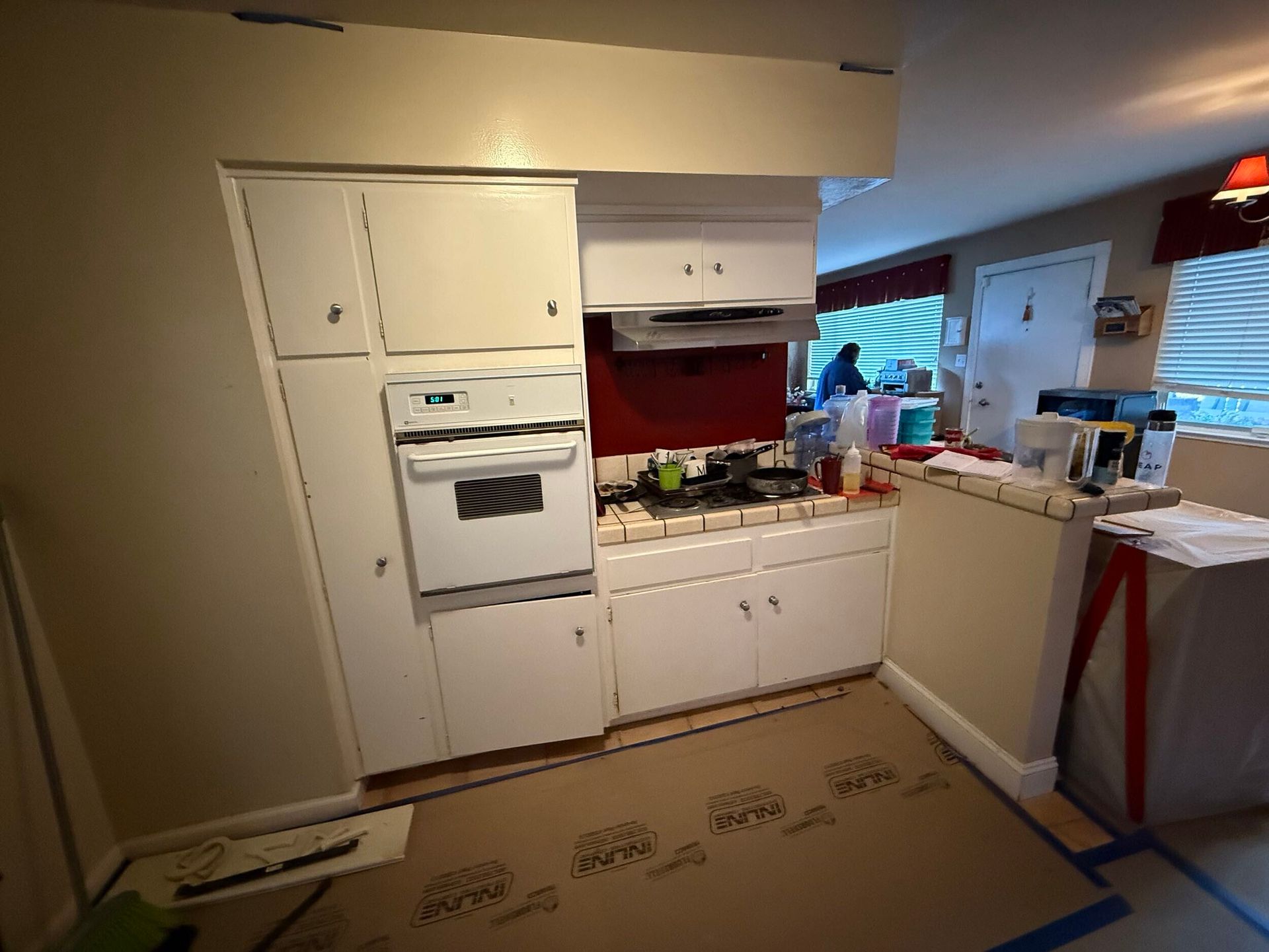 Modern kitchen remodel featuring gray shaker-style lower cabinets, white upper cabinets, quartz countertops with subtle veining, stainless steel appliances, built-in oven, sleek black cooktop, contemporary range hood, and textured stone tile backsplash. Renovation completed by Dream Build Services, showcasing high-quality craftsmanship, modern design, and functional layout for residential kitchen remodeling.