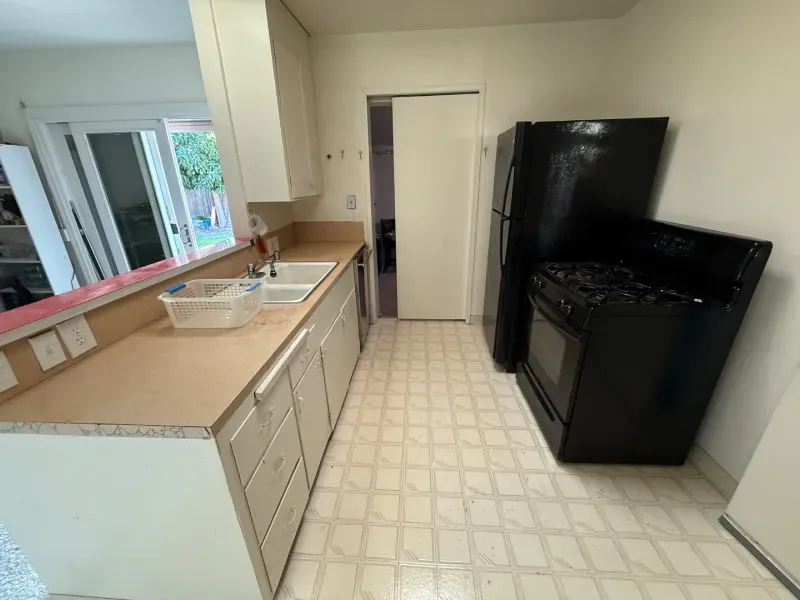 A kitchen with a black stove , refrigerator and sink.