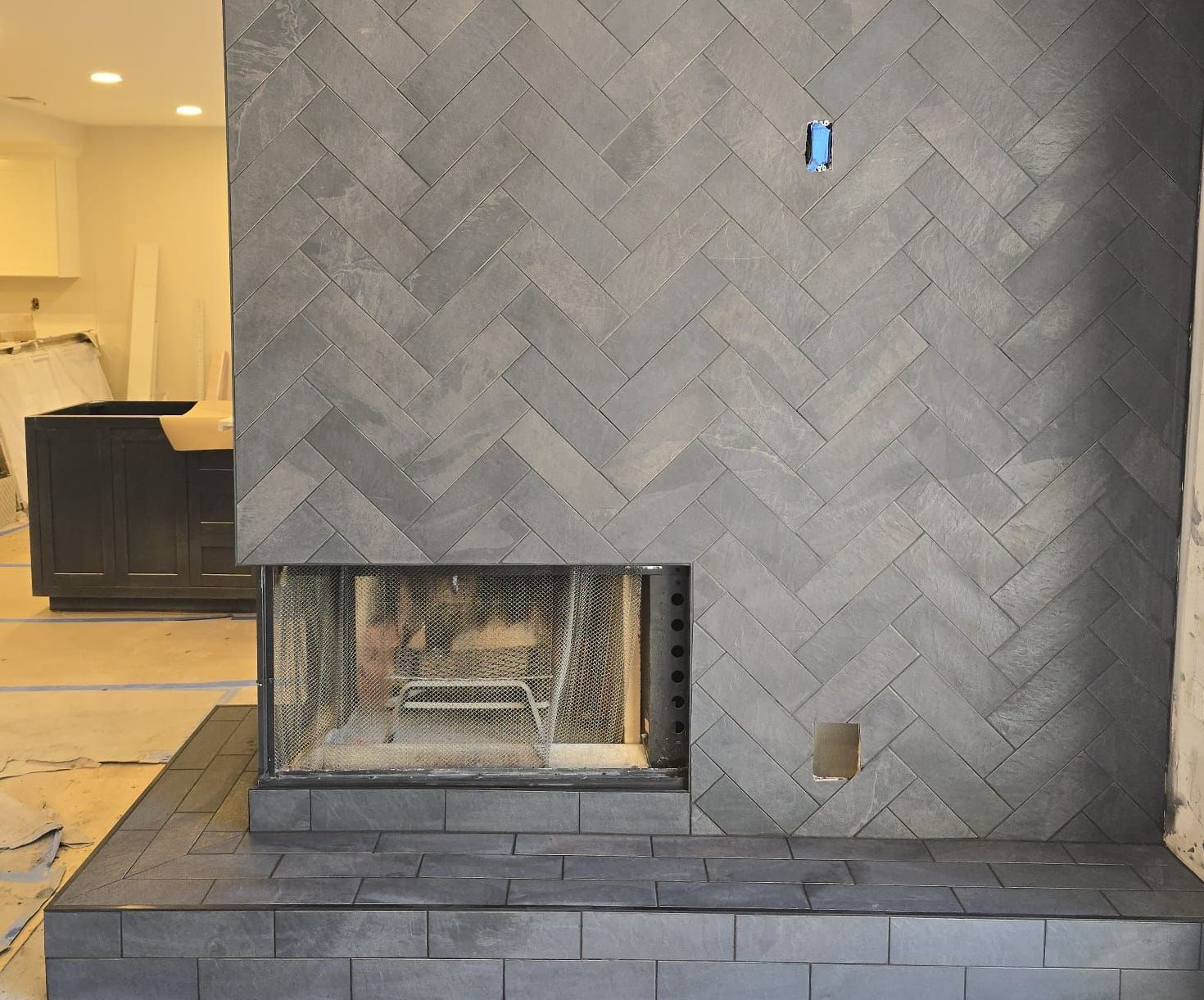 A modern fireplace with a herringbone brick pattern in shades of gray. The fireplace sits in a room under construction.