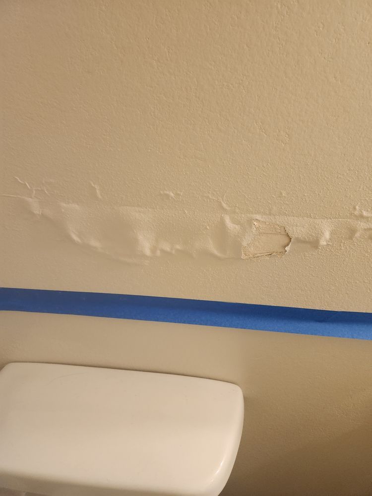 A toilet in a bathroom with a blue tape on the wall.