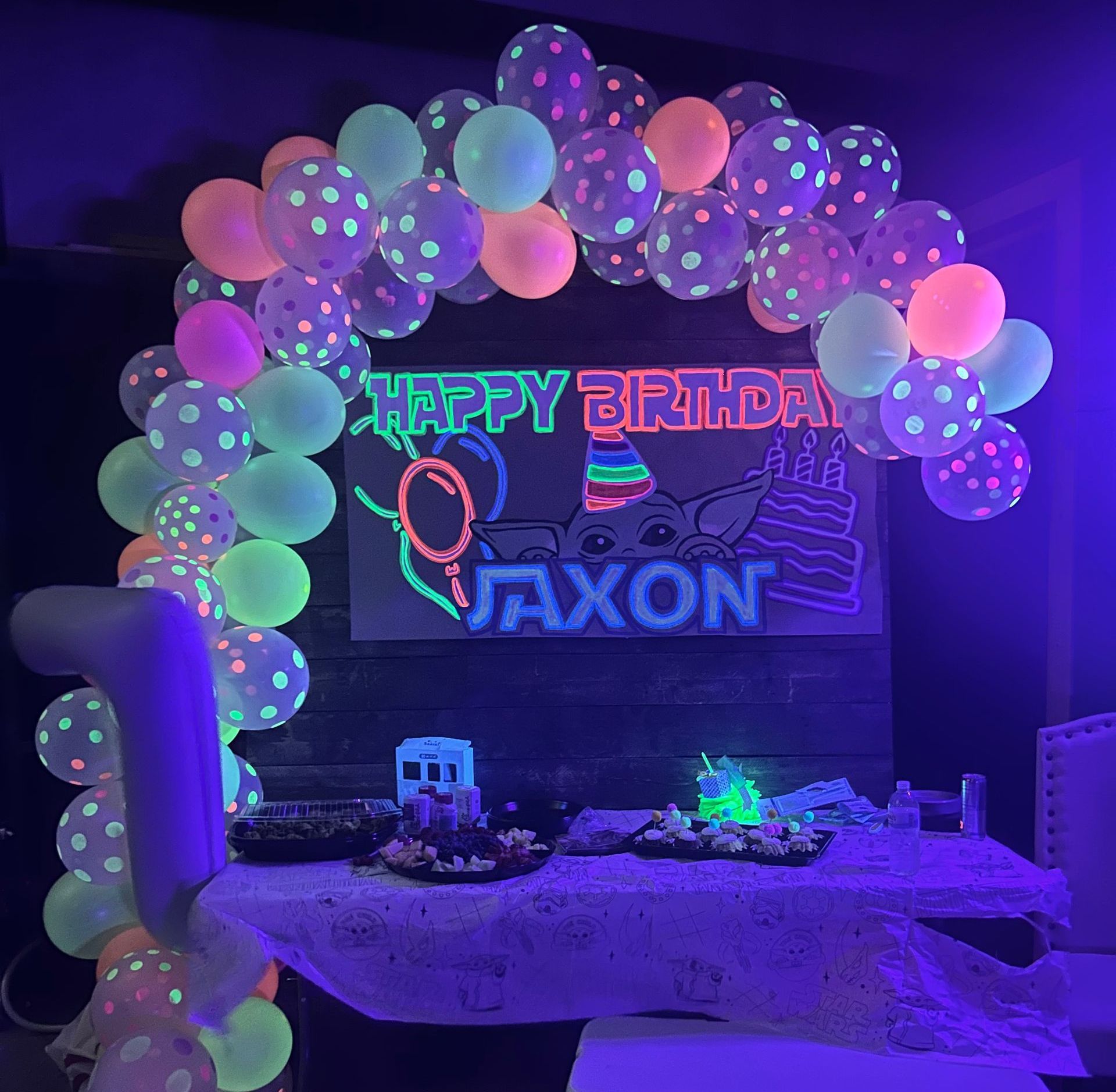 A birthday party with glow in the dark balloons and a neon sign.