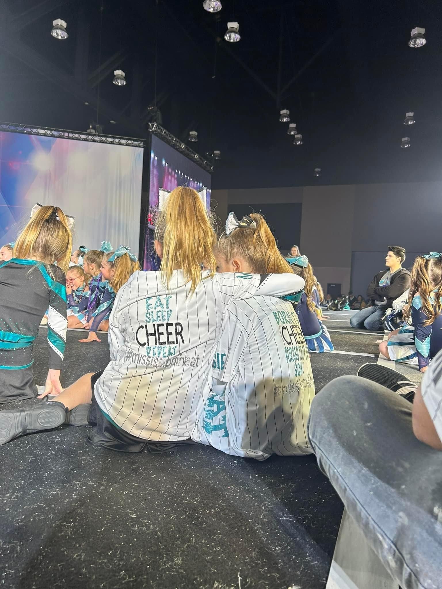 A group of cheerleaders are sitting on the floor in front of a large screen.