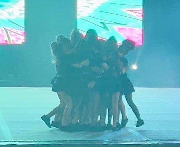 A group of women are dancing on a stage in front of a large screen.