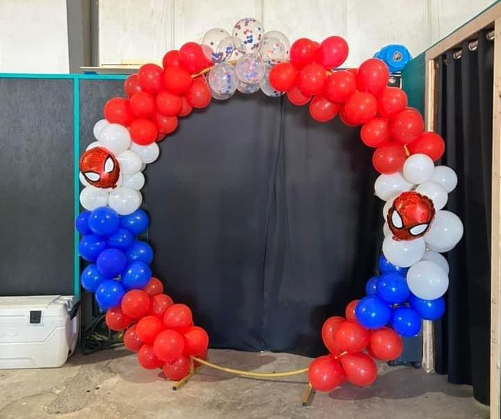 A red , white and blue balloon arch with a spider man head on it.