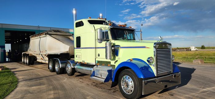 Light green and blue semi-truck hauling a trailer with a light colored load.