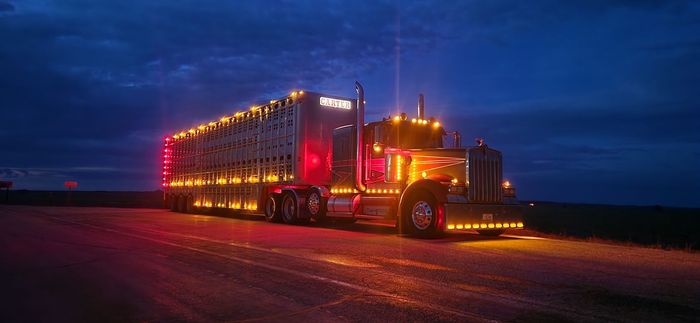 Semi-truck with numerous lights on a dark road at night.