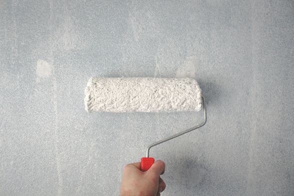 Hand painting a light blue wall with a white paint roller, red handle.
