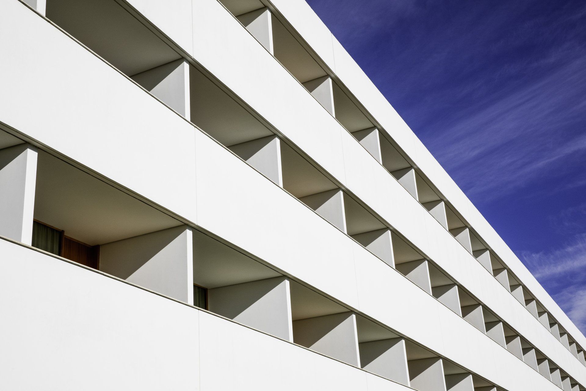 Exterior de edifício branco com varandas abertas repetidas contra um céu azul.