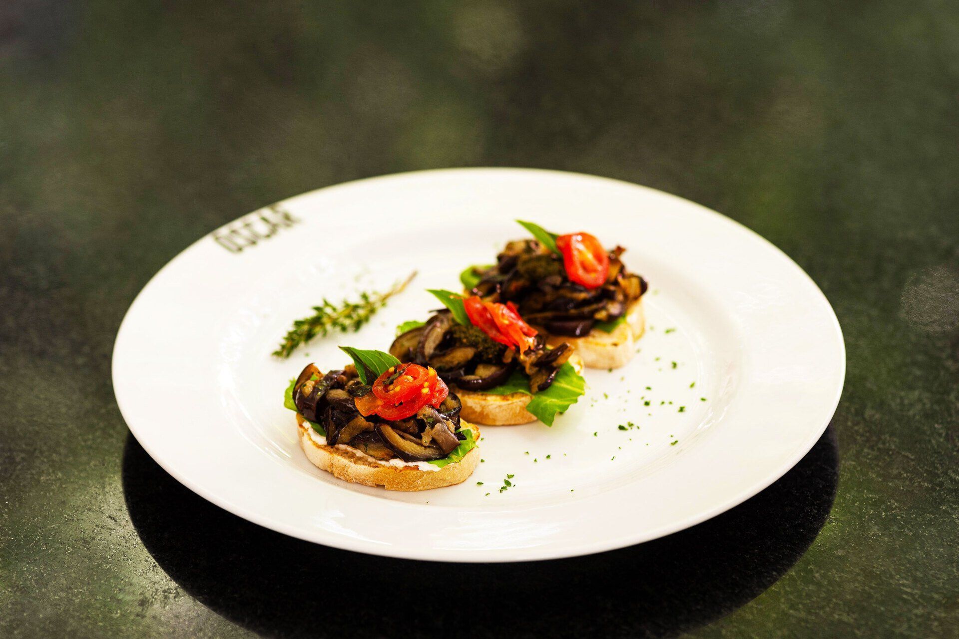 Bruschetta de três cogumelos em um prato branco, decorada com manjericão e tomates.