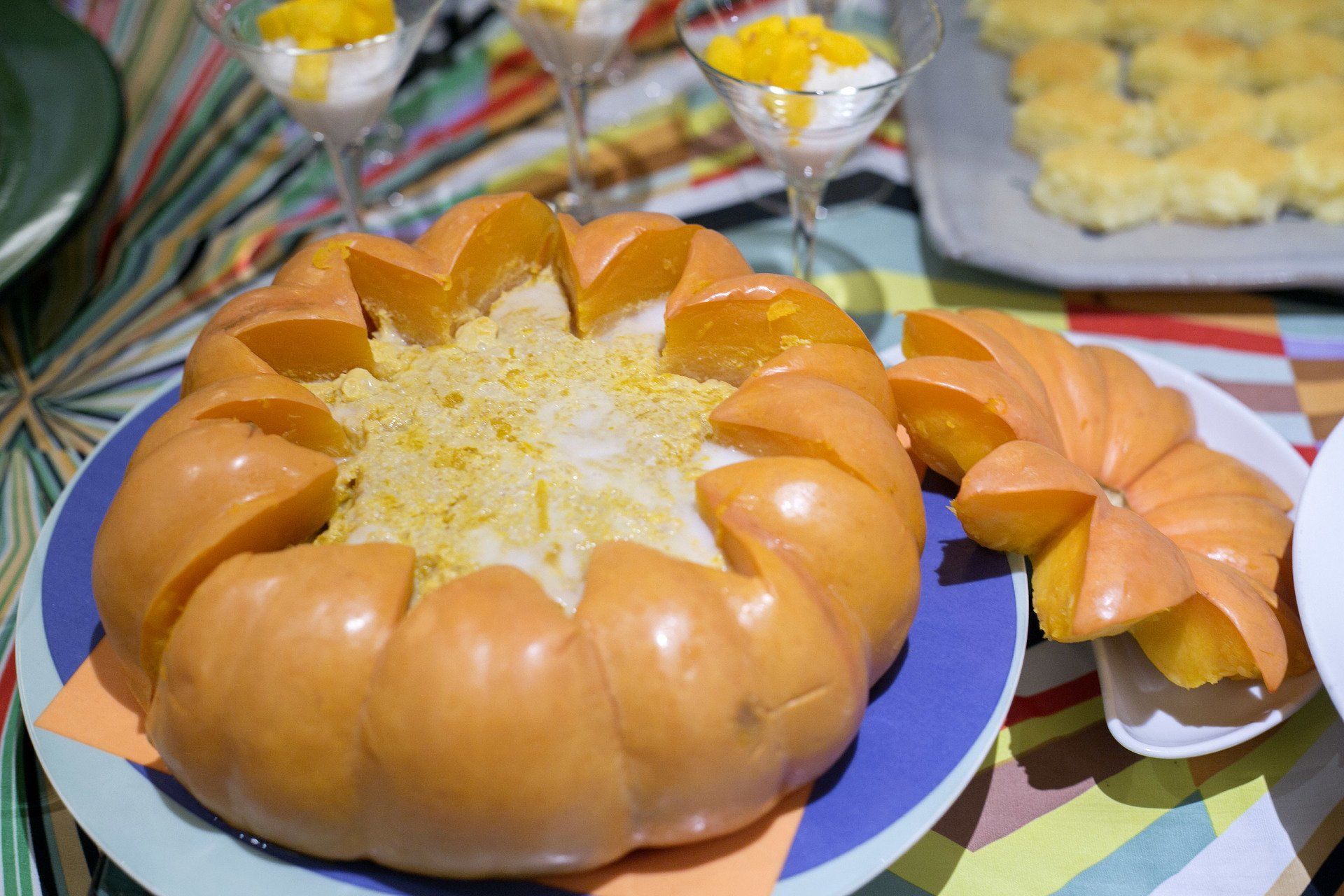 Prato de abóbora com arroz, fatias cortadas. Sobremesas de manga ao fundo.
