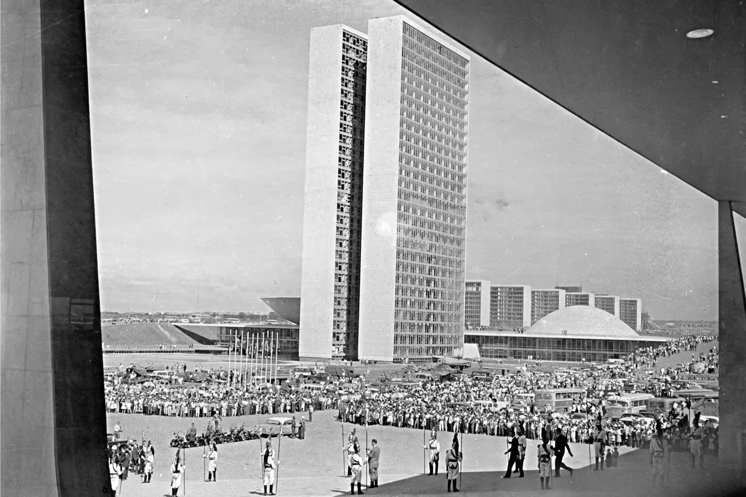 Quarto de hotel aconchegante com cama king-size, bancos, luminárias e uma estante iluminada decorativa.