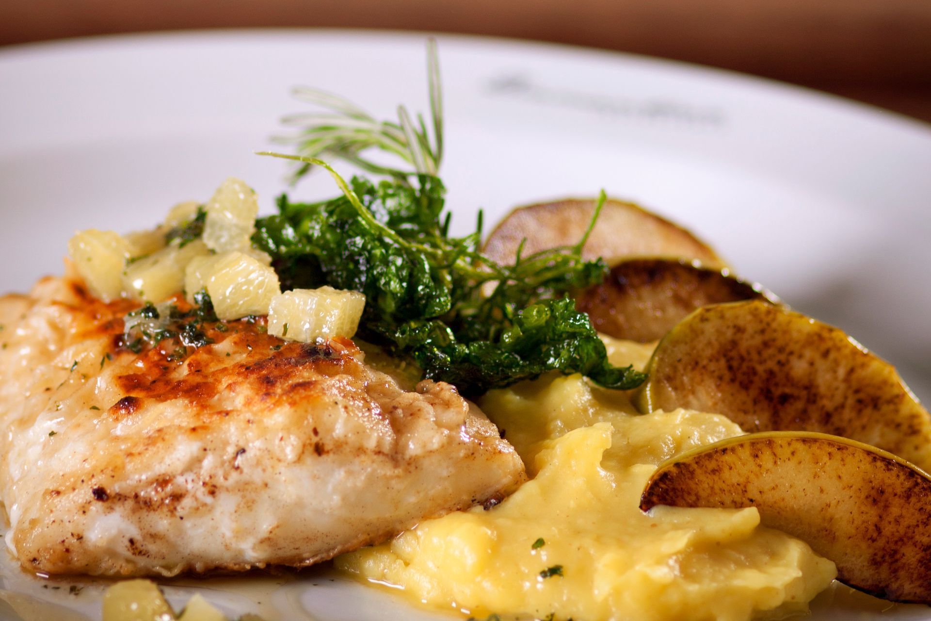 Filé de peixe grelhado em purê amarelo, coberto com salsa de maçã em cubos e couve frita, com fatias de maçã.