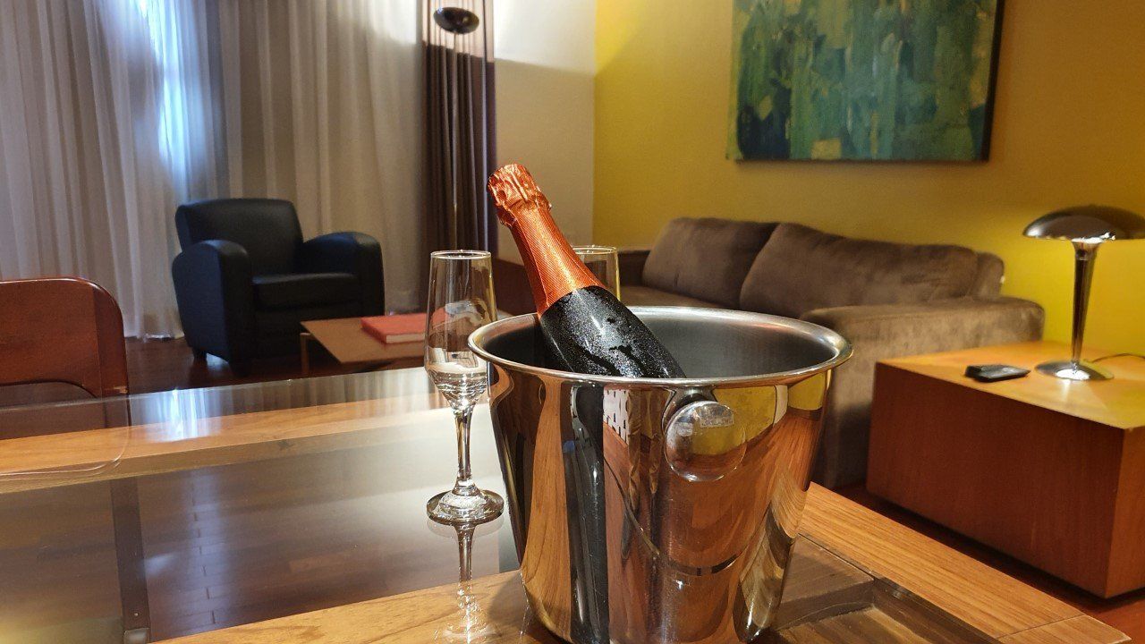 Balde de champanhe com garrafa e taça sobre a mesa; sala de estar com sofá, poltrona e arte.