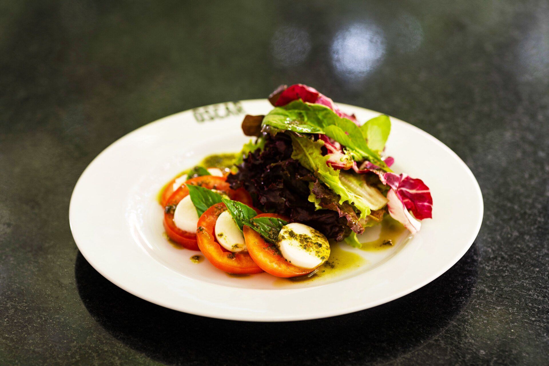 Salada com tomates, mussarela e verduras em um prato branco.