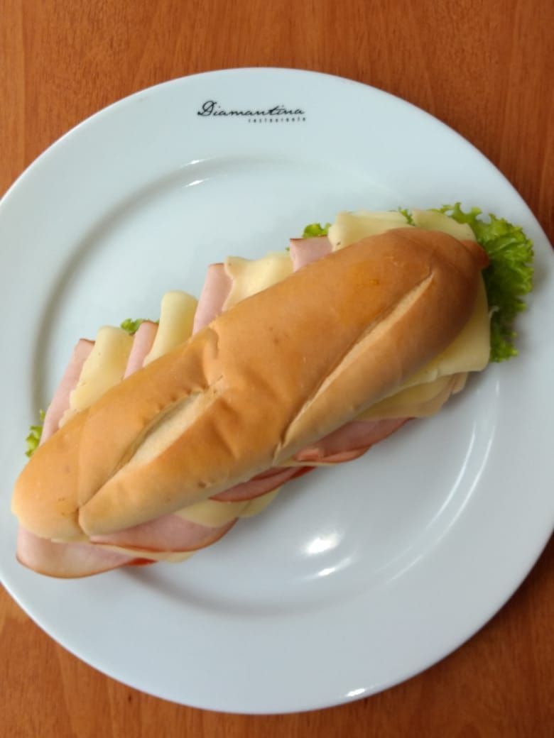 Sanduíche em um prato branco: presunto e queijo, alface, em uma baguete.