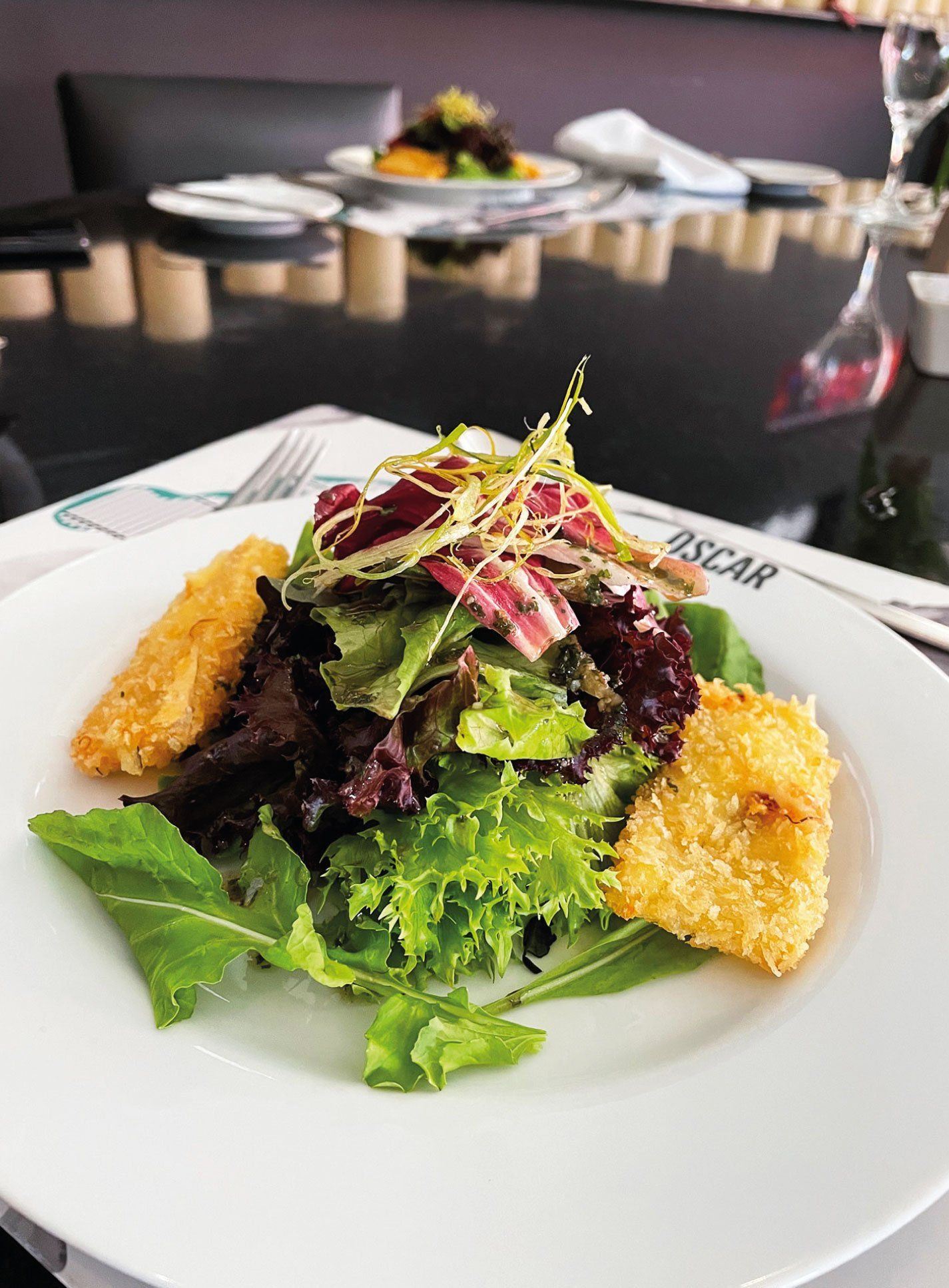 Salada com queijo frito em um prato branco em um restaurante.