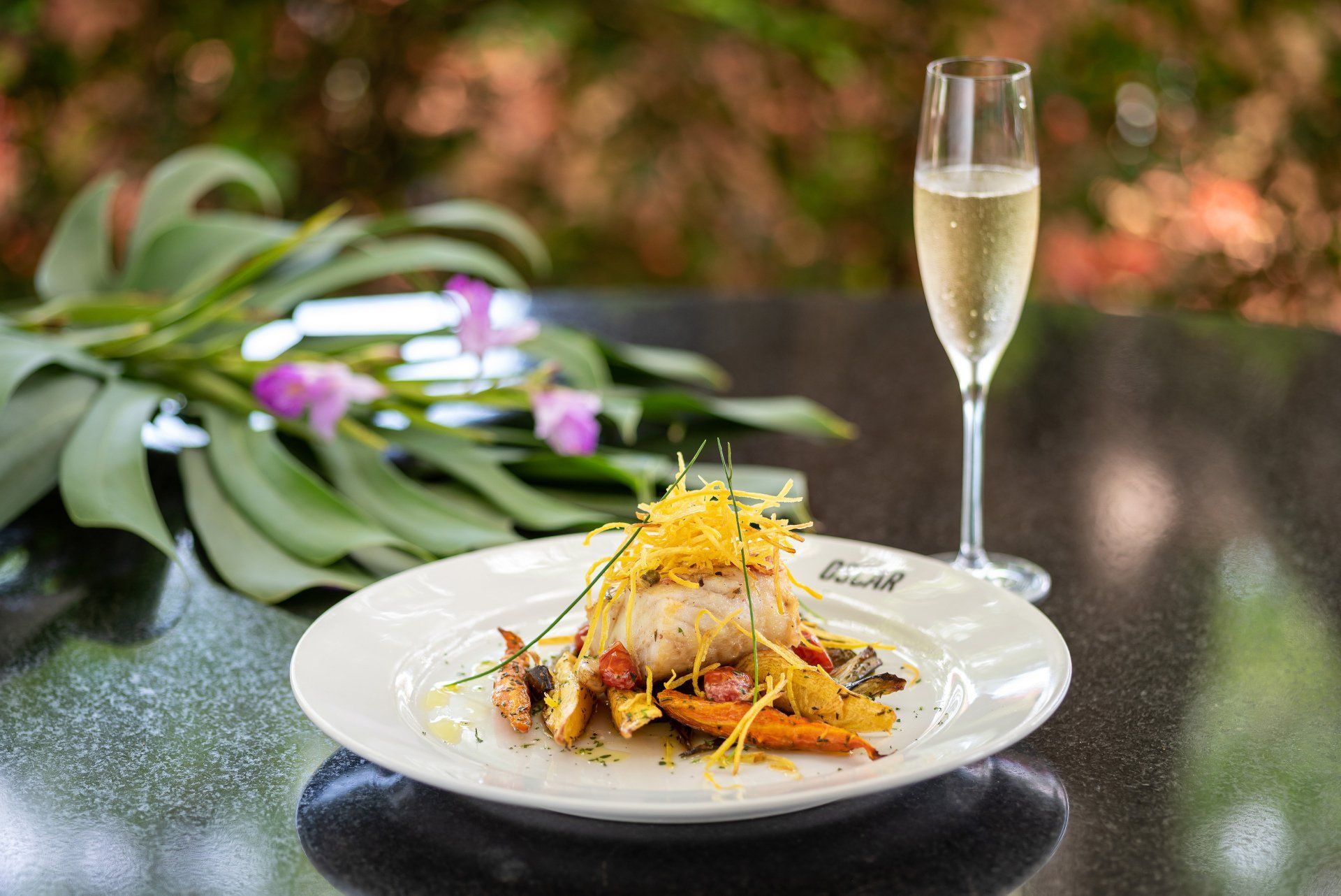 Prato de comida com vegetais e uma taça de champanhe em uma mesa ao ar livre.