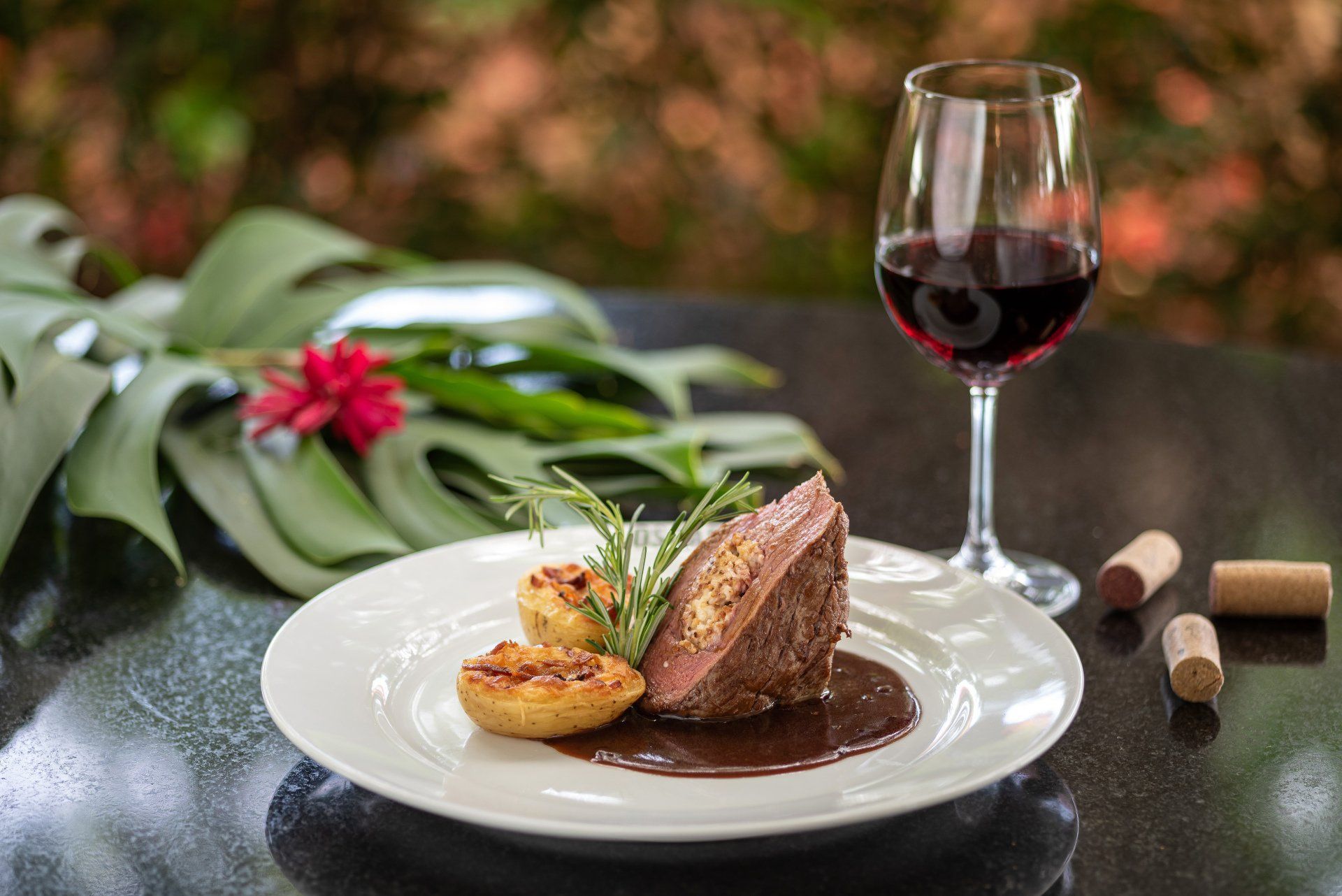 Bife com batatas assadas e vinho tinto, apresentado ao ar livre, com rolhas.