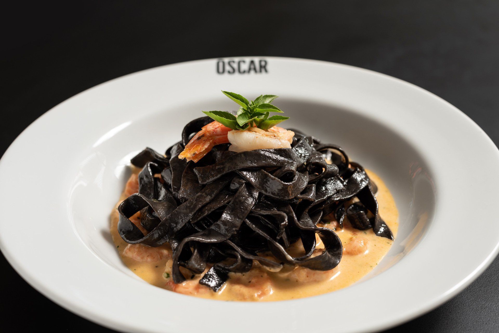 Macarrão preto com camarão e manjericão em uma tigela branca com a etiqueta 