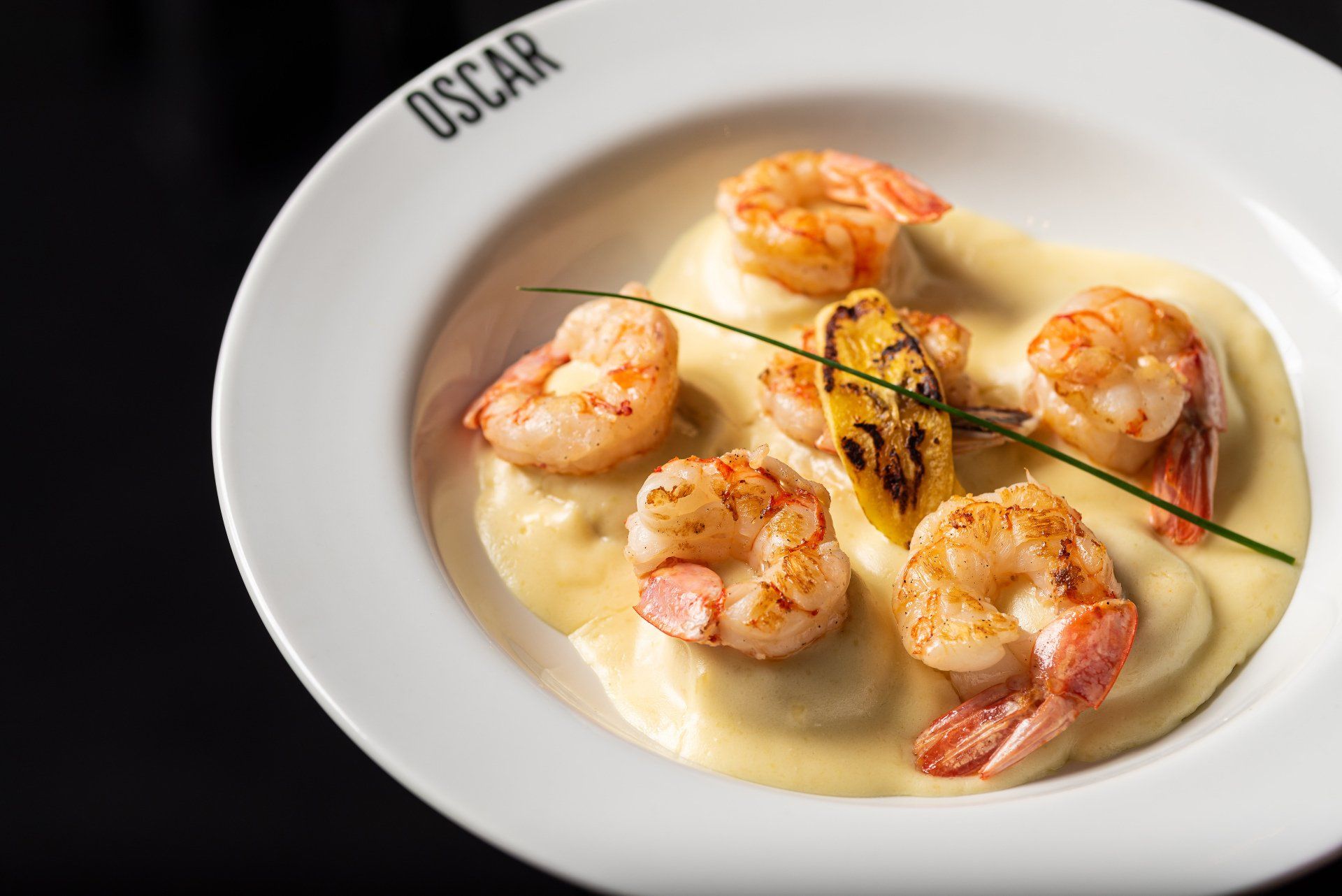 Prato de camarão e ravióli em molho cremoso; guarnecido com limão e um raminho de cebolinha.