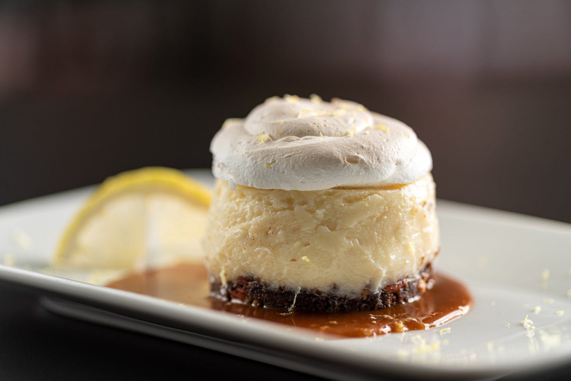 Cheesecake de limão com cobertura de merengue e calda de caramelo em um prato branco.
